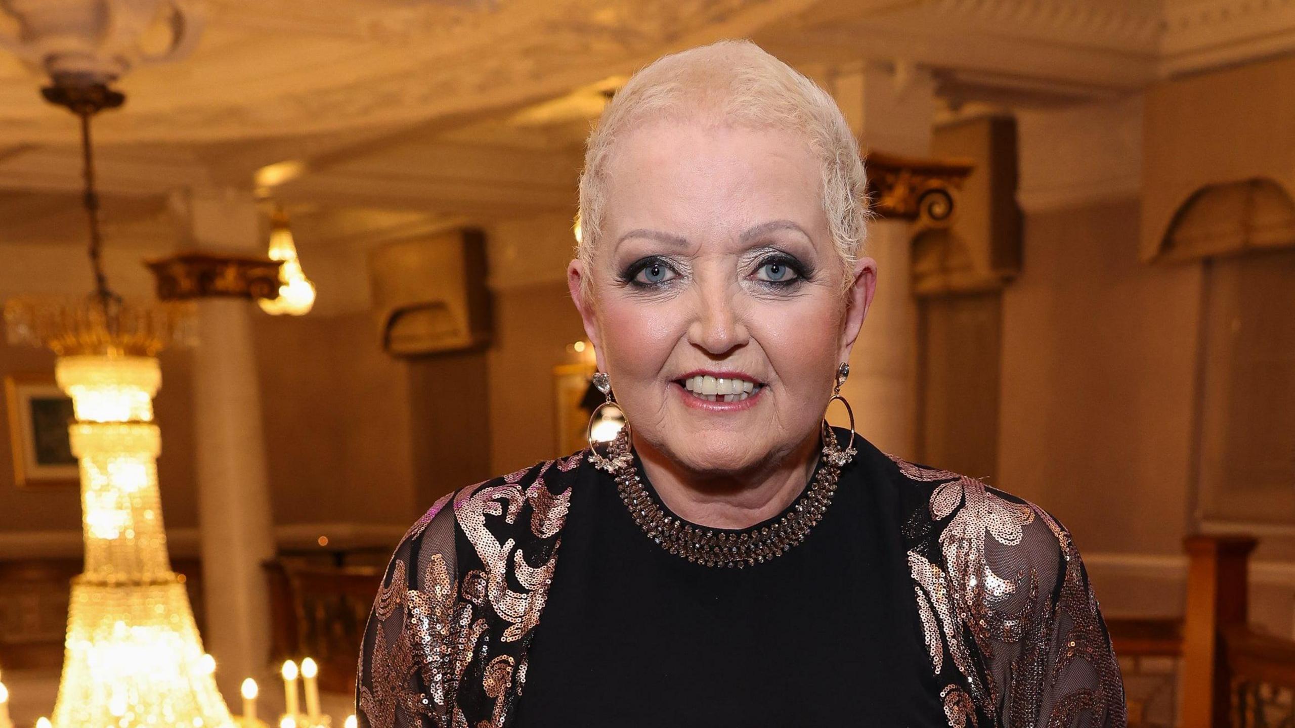 Linda Nolan wearing a black and gold glittery top with short blonde hair