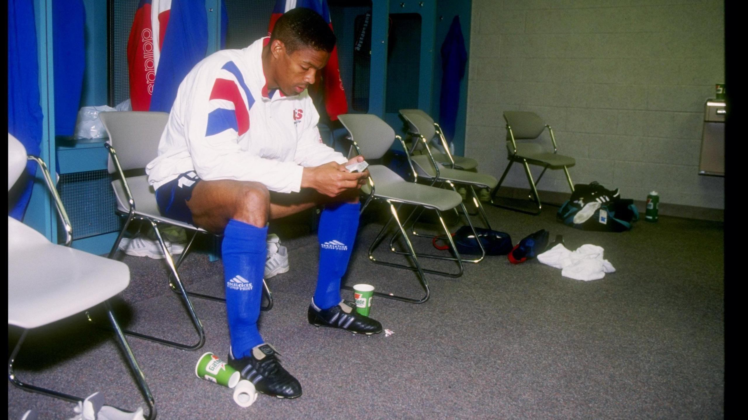 Desmond Armstrong sits in the locker room in team kit, with litter at his feet and sports kit on the floor