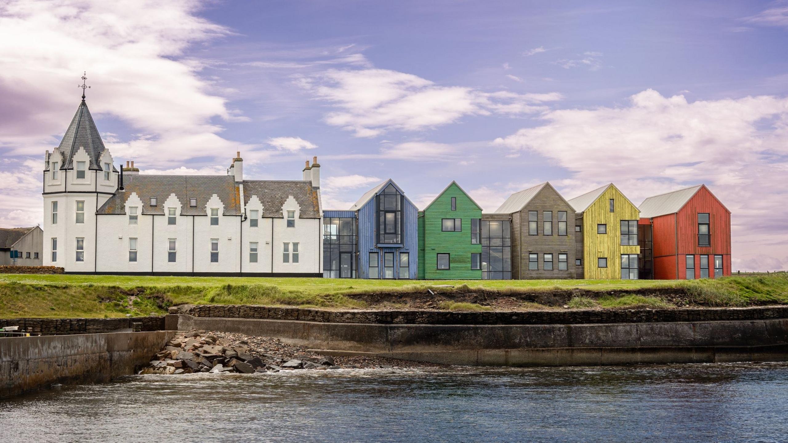 A clear sky over a redeveloped hotel at John O'Groats harbour. The original white hotel now has a colourful Norse-style extension, with a blue, green, brown, yellow and red frontage.