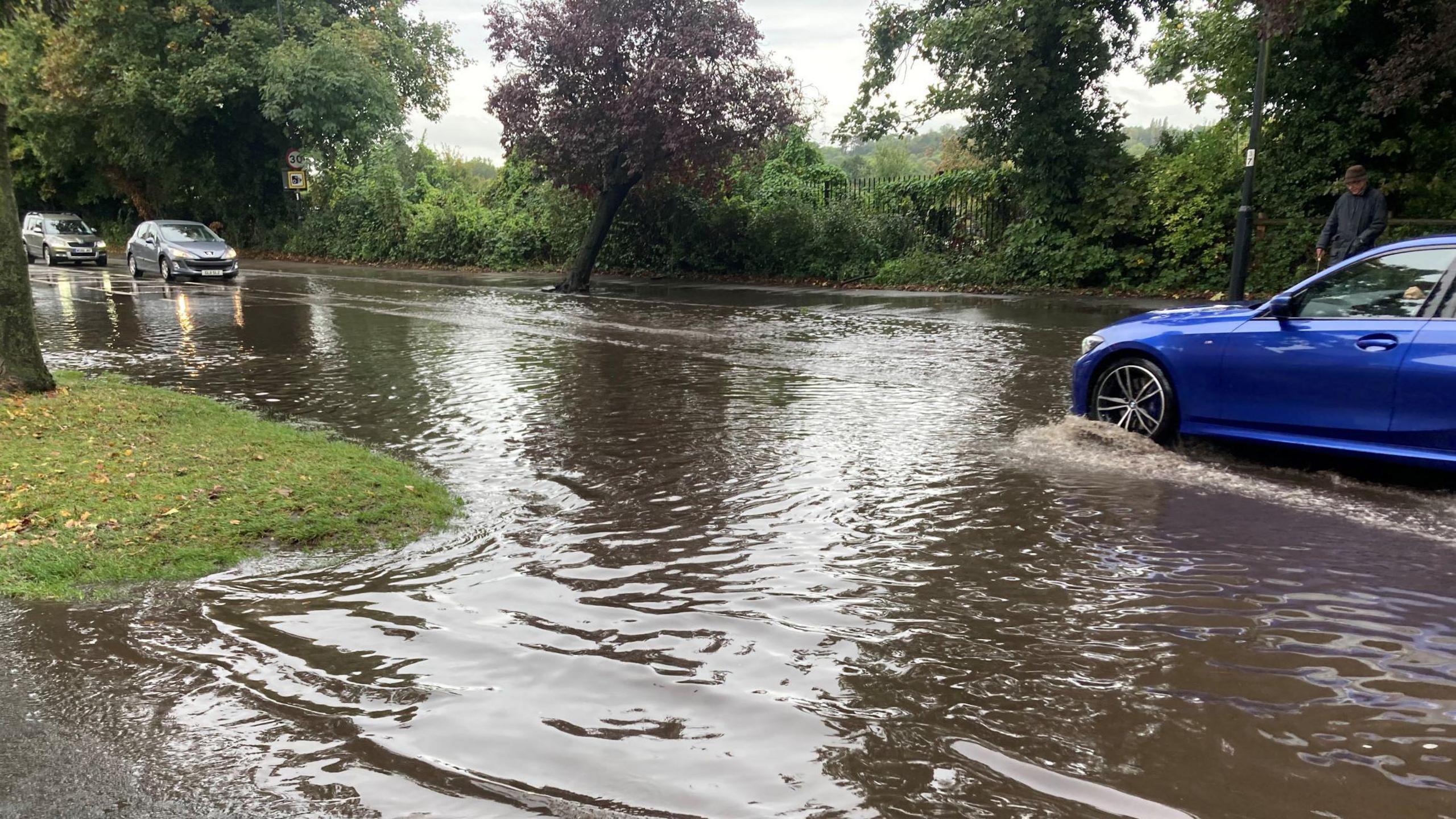 A flooded road with a blue car driving through the water 