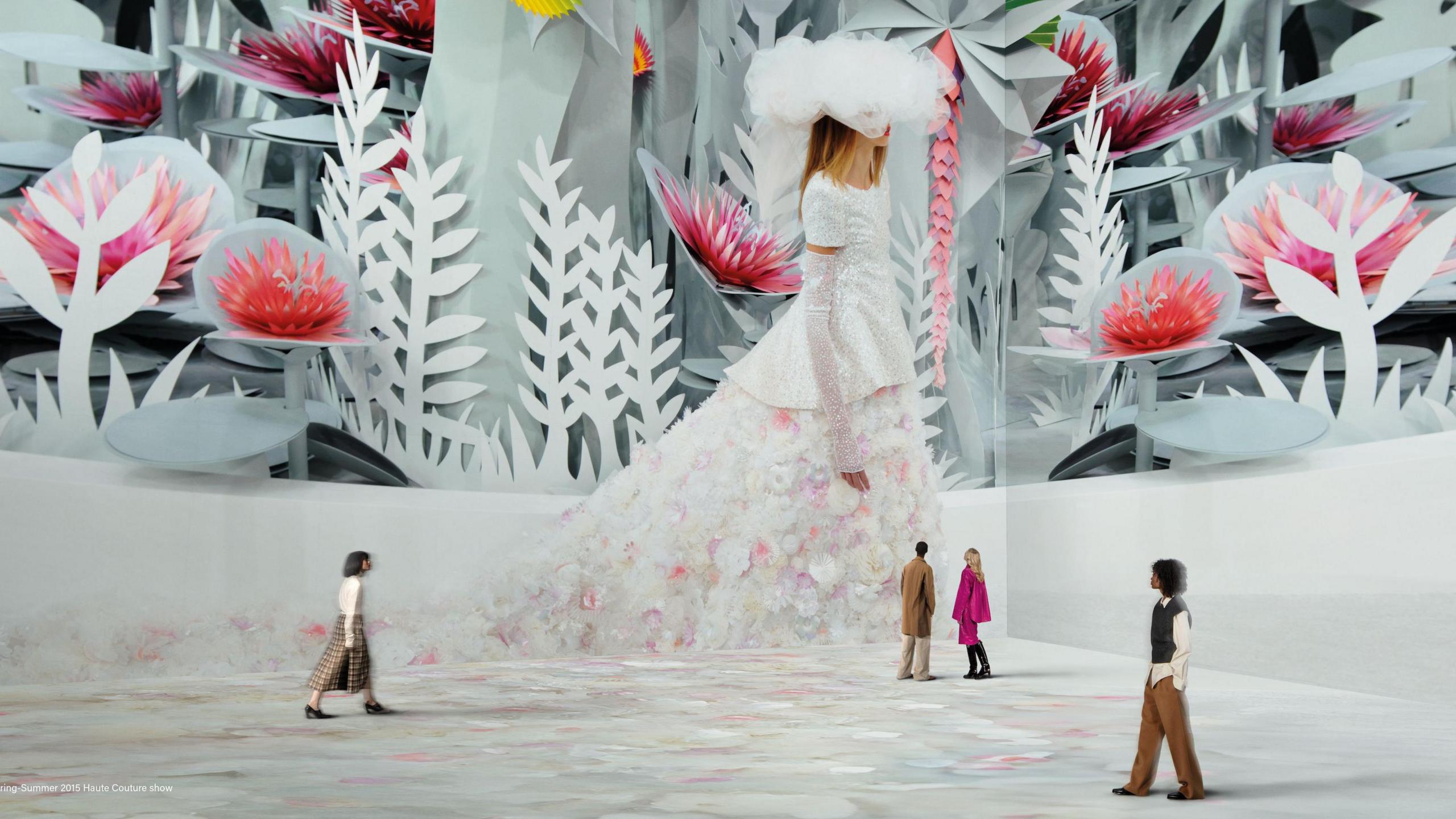 Four people in the Lightroom, dwarfed by a projection of a fashion model wearing a white hat and a white dress with a long floral train