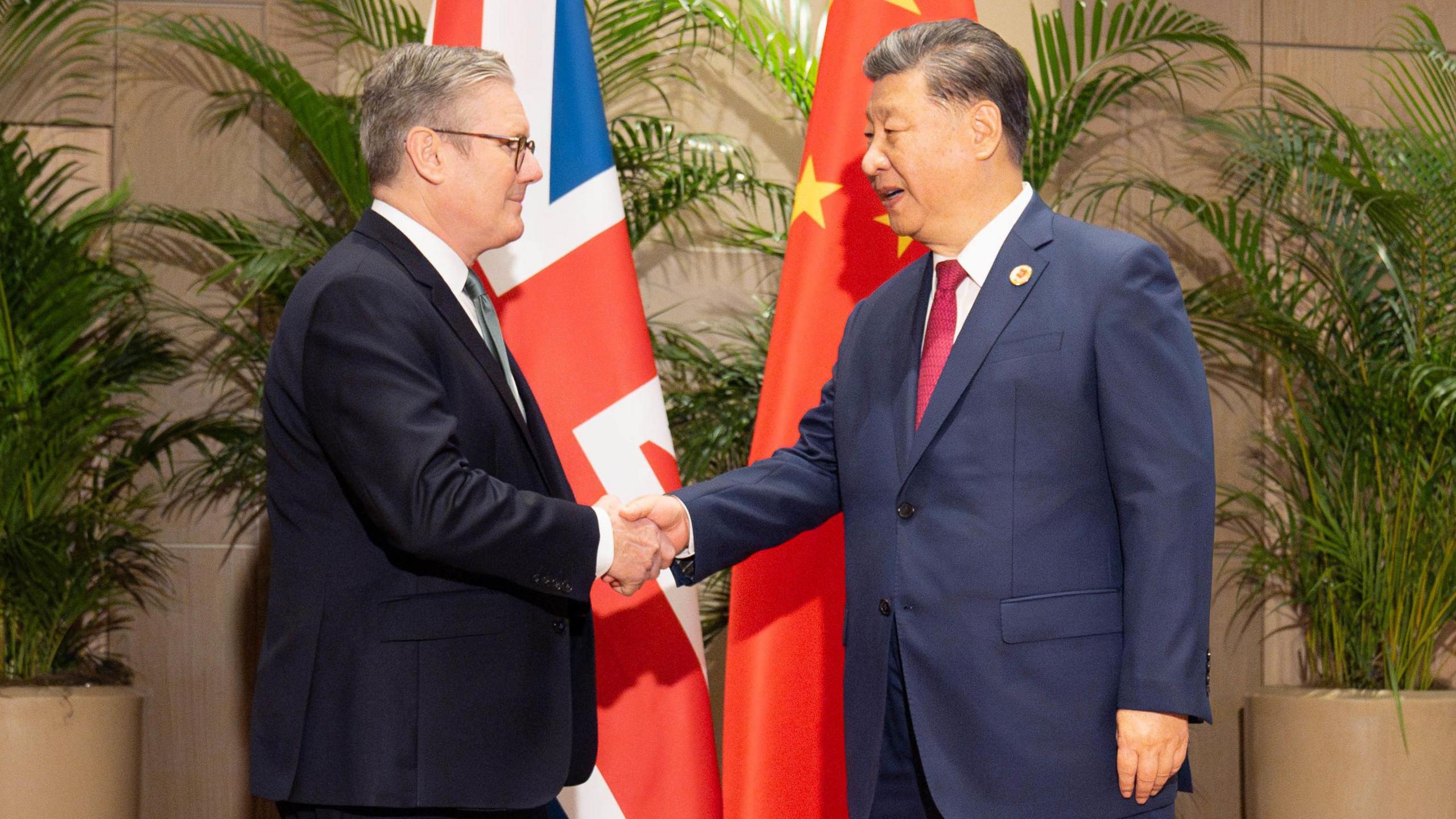 Prime Minister Sir Keir Starmer shaking hands with President Xi Jinping in front of a British and Chinese flag. 