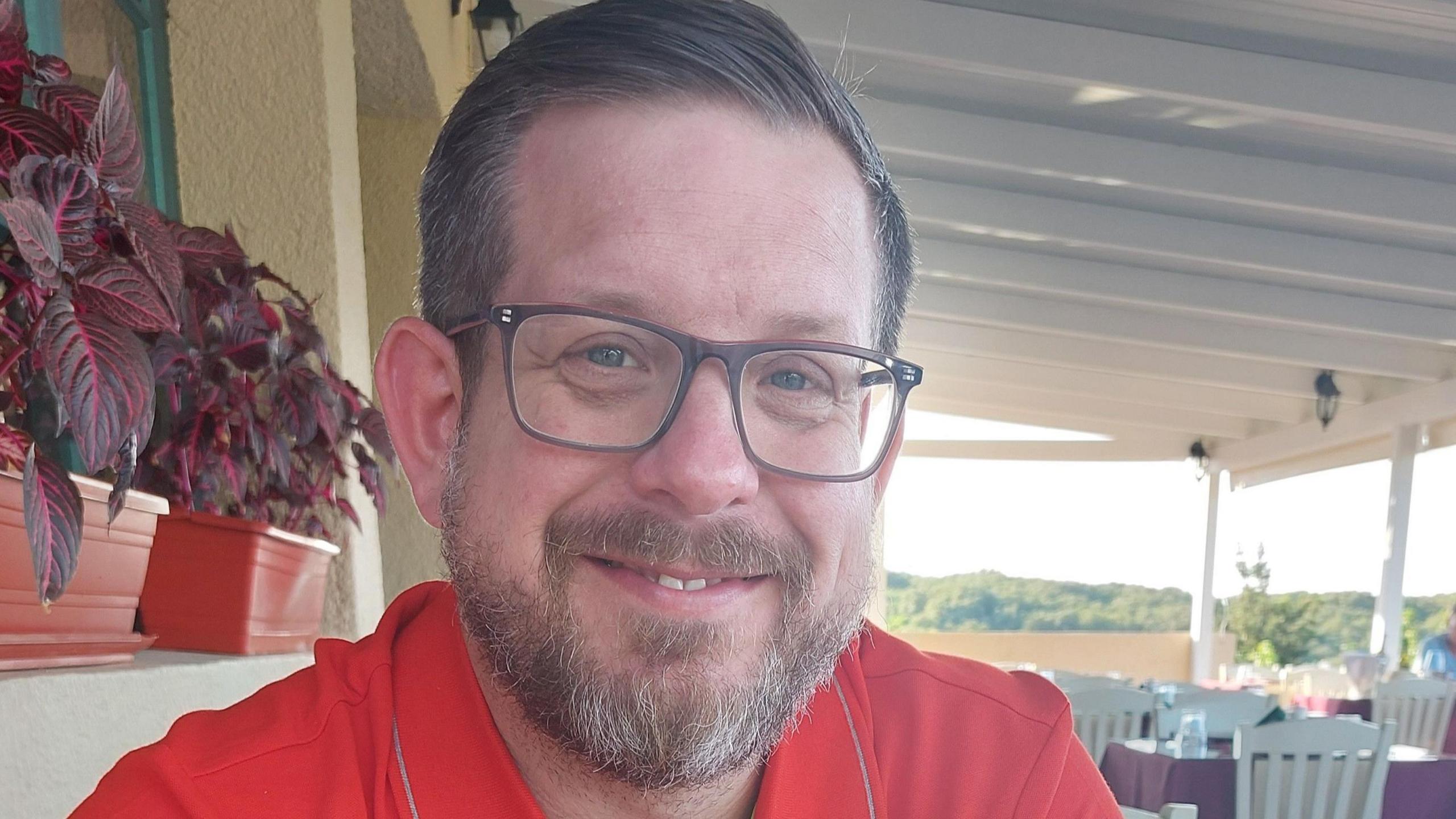 Man smiling at the camera wearing glasses and a red top