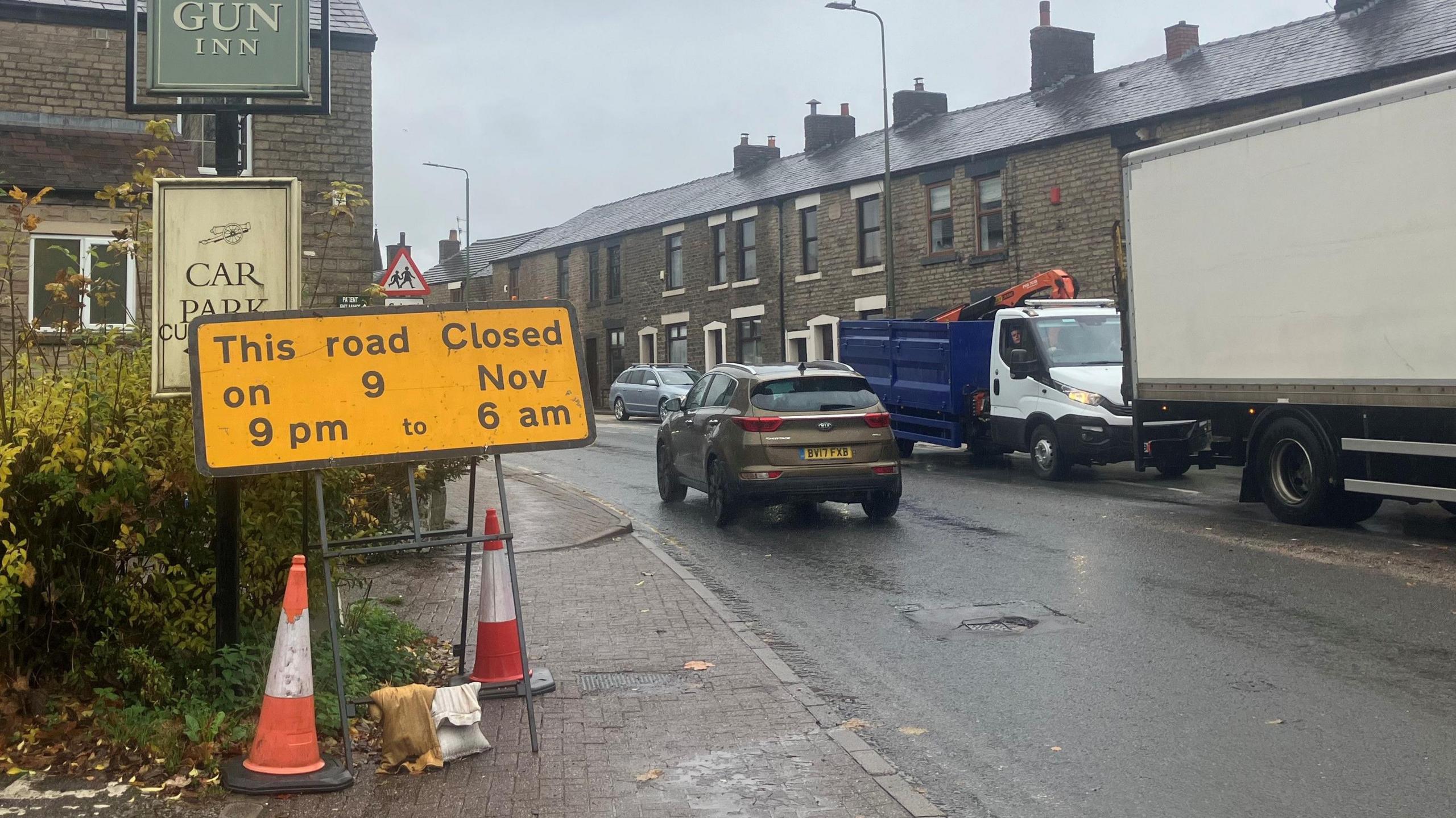 Photograph of a road sign at The Gun Inn traffic lights in Longdendale. The image shows cars, a wagon and a lorry.