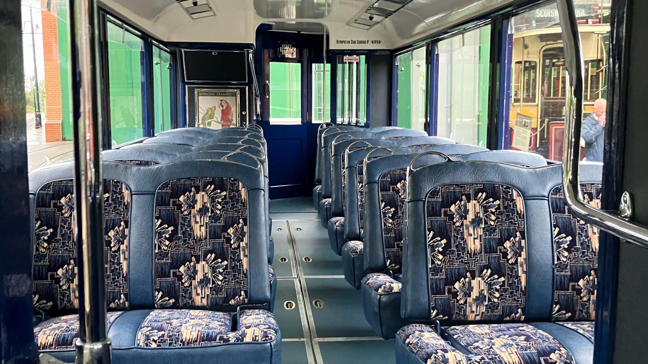 Rows of blue leather seats inside a 1950s tram. The seats are laid out in sets of two on each side of the carriage walkway.