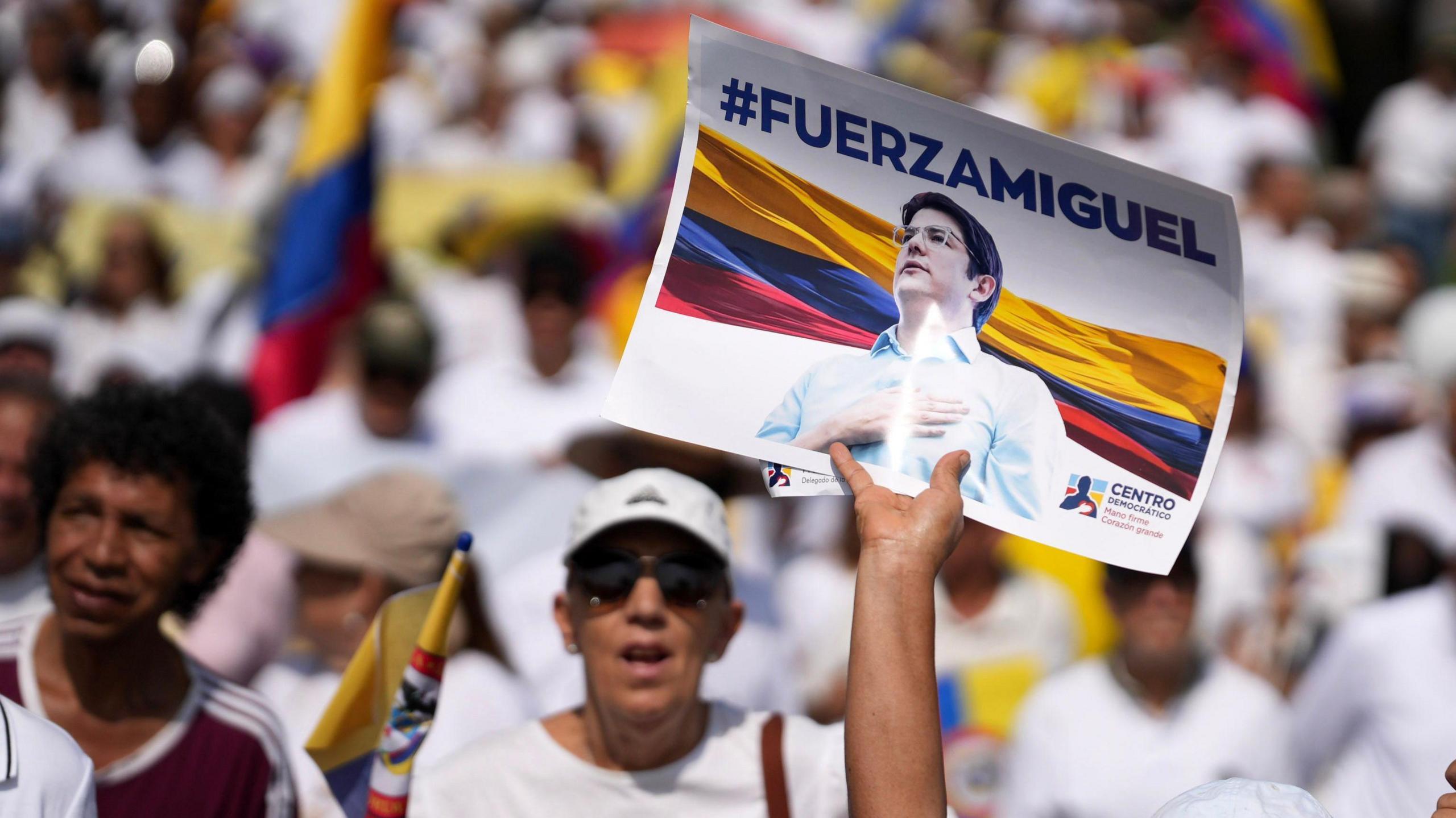 A person holds up a sign with Miguel Uribe Turbay's face on it