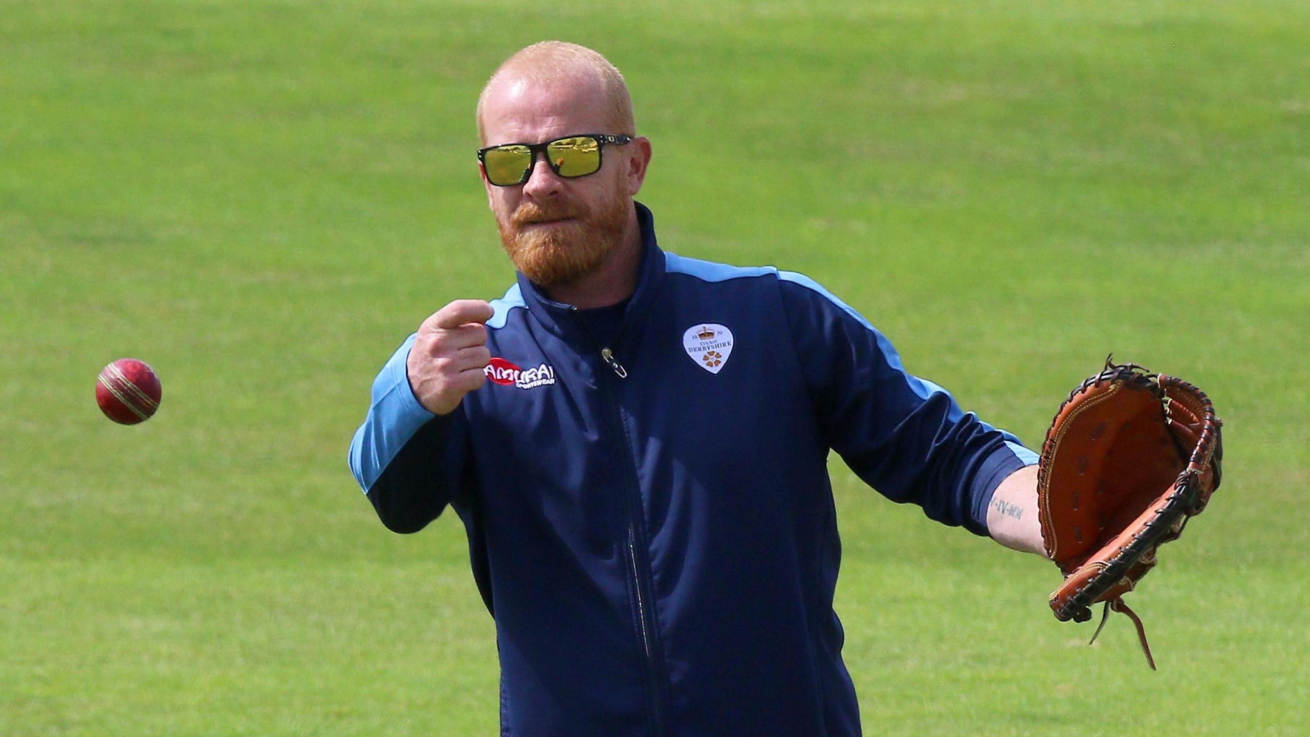 Graeme Welch in sunglasses and wearing a mitt throws the ball during a fielding routine