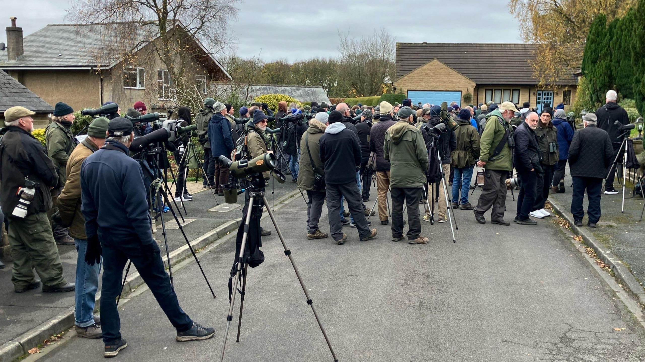 A large group of people standing in a street carrying cameras and telescopes