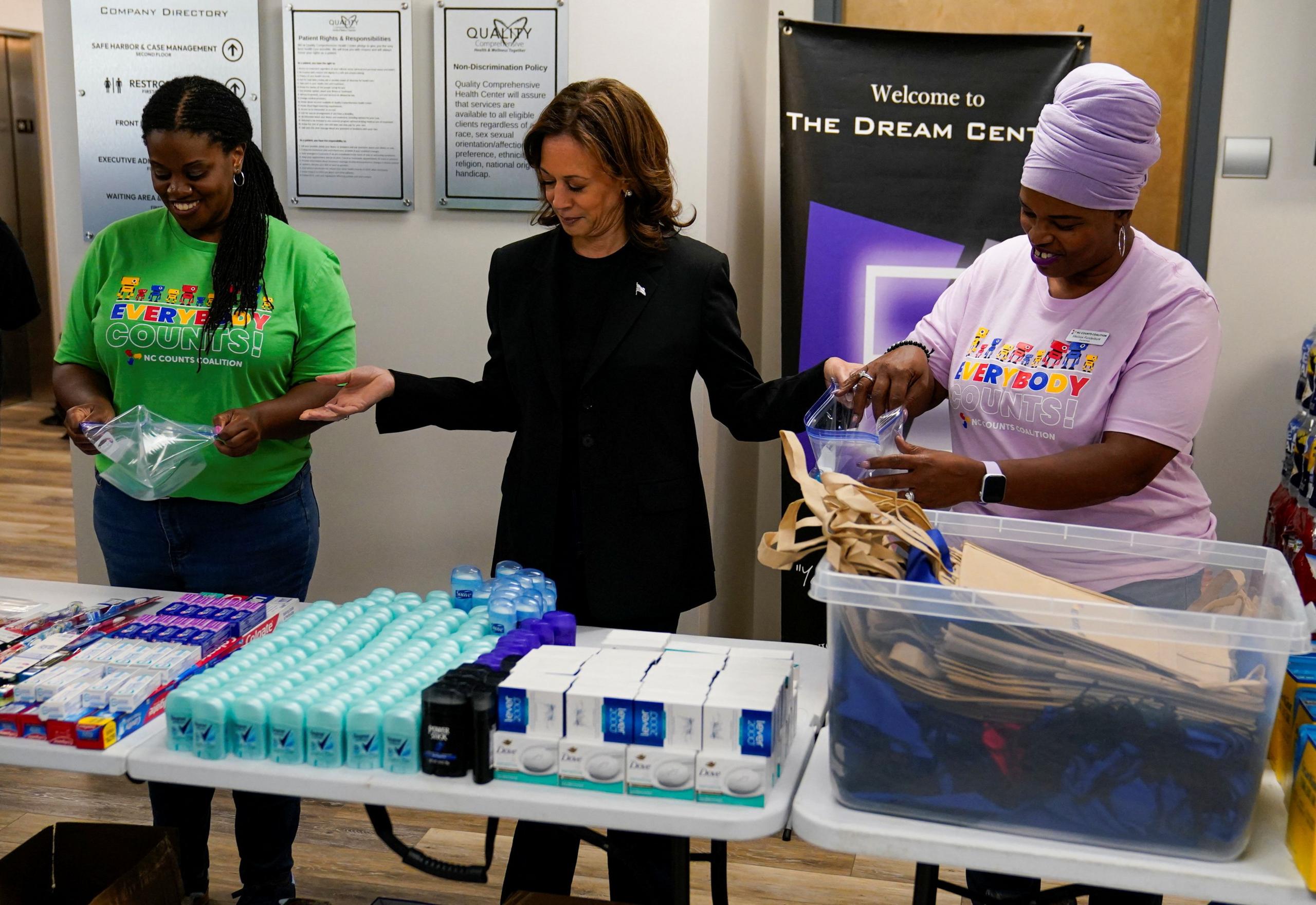 Kamala Harris flanked by emergency aid workers looking at essential supplies laid out on tables in North Carolina