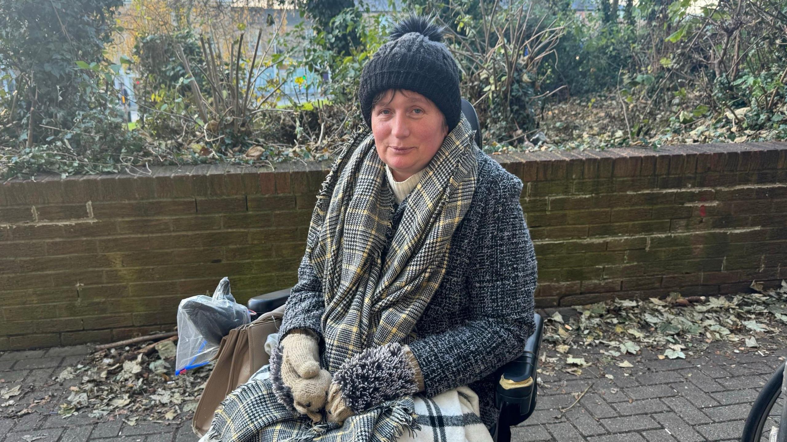 Michelle, dressed in a coat, scarf, woolly hat and gloves, sits in an electric wheelchair outside the Jobcentre in York.