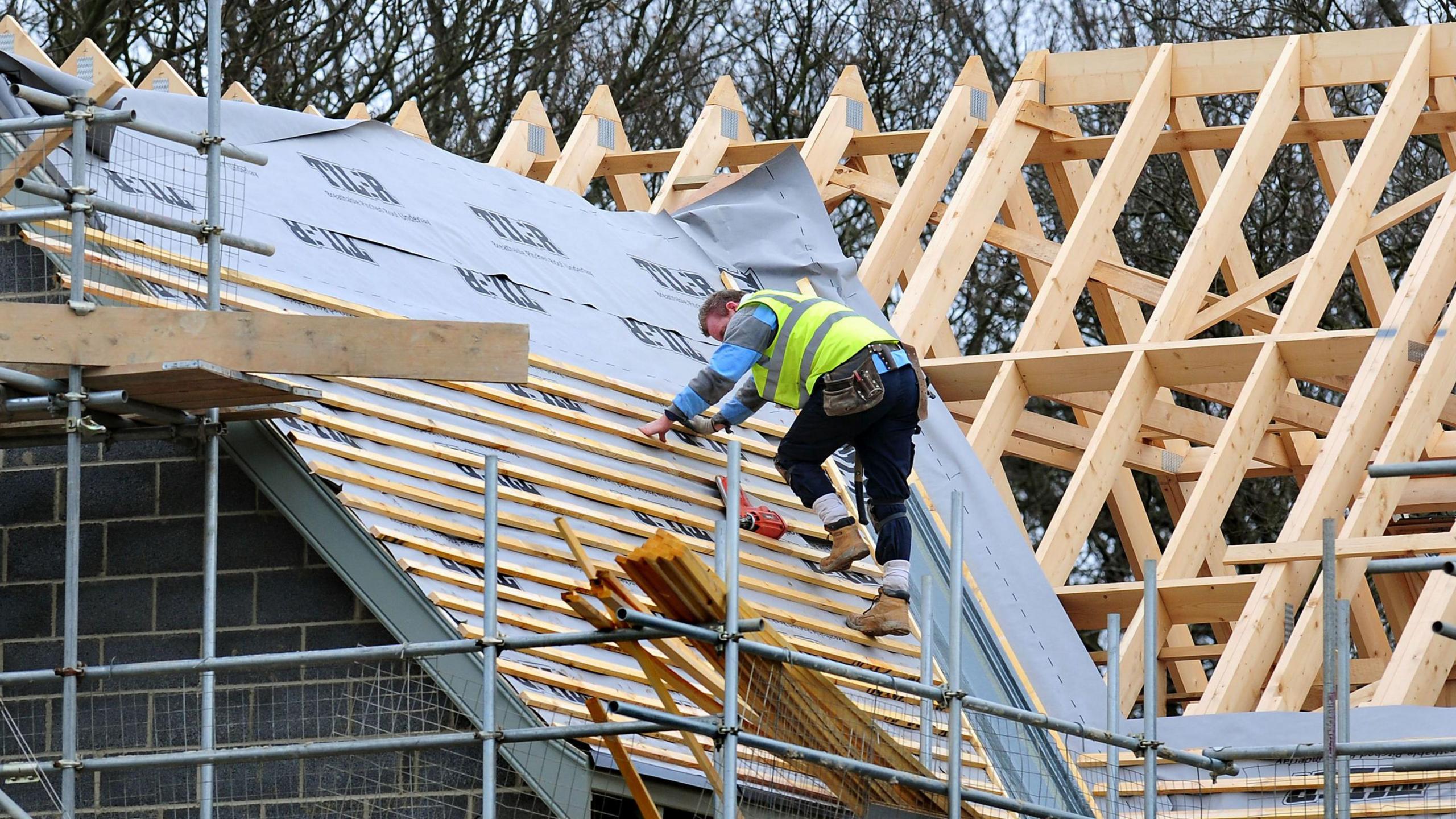 A roofer is wearing a high-res jacket and he is carrying out building work on the roof of a property. 