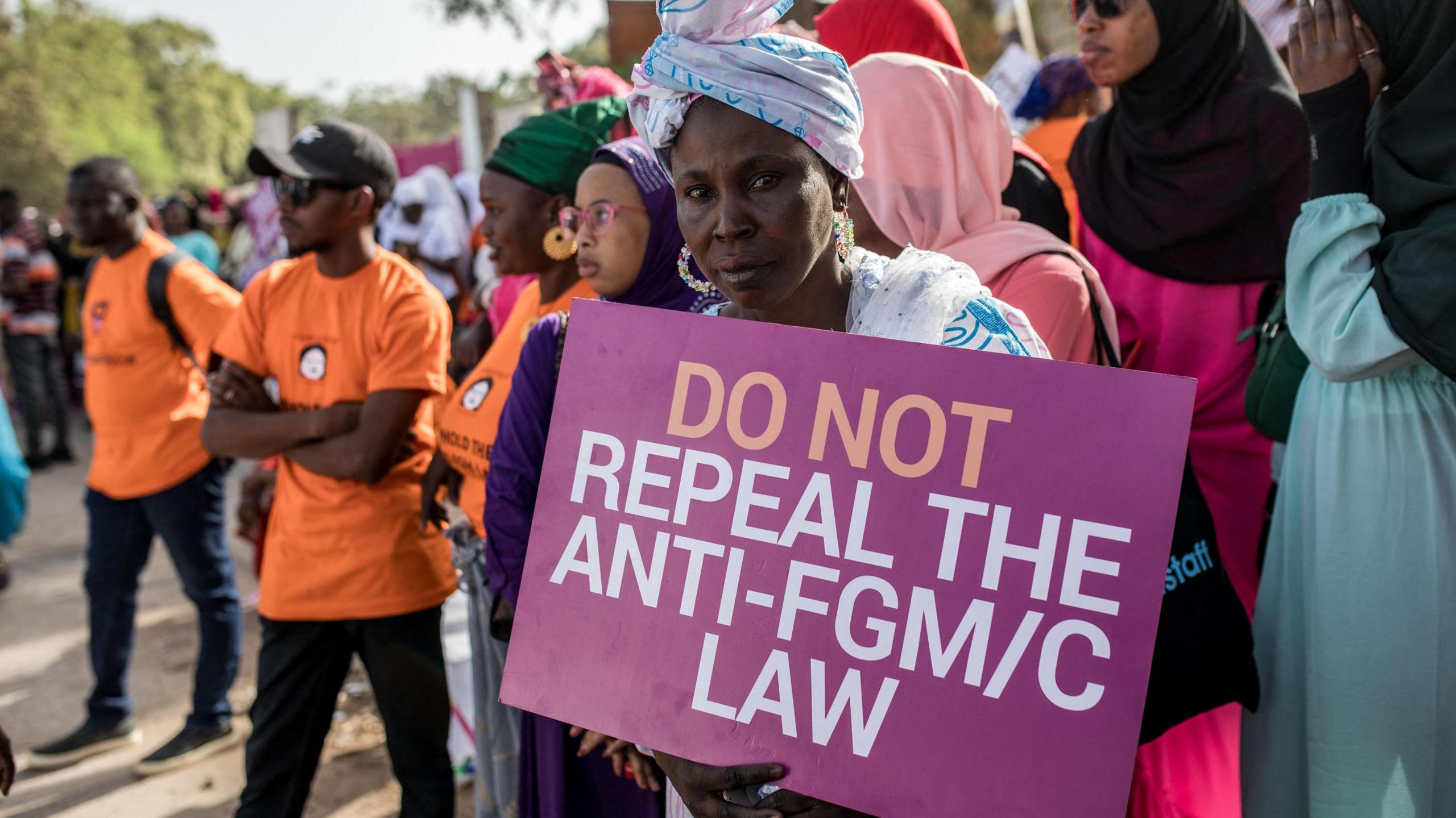 An anti Female Genital Mutilation (FGM) protester holds a placard outside the National Assembly in Banjul on march 18, 2024, during the debate between lawmakers on a highly controversial bill seeking to lift the ban on FGM. Gambian lawmakers voted on March 18, 2024 to advance to the next parliamentary stage a highly controversial bill that seeks to lift a ban on female genital mutilation (FGM), which has been in place since 2015. The issue has divided the tiny West African nation for months, with hundreds gathering to protest outside parliament. (Photo by MUHAMADOU BITTAYE / AFP) (Photo by MUHAMADOU BITTAYE/AFP via Getty Images)