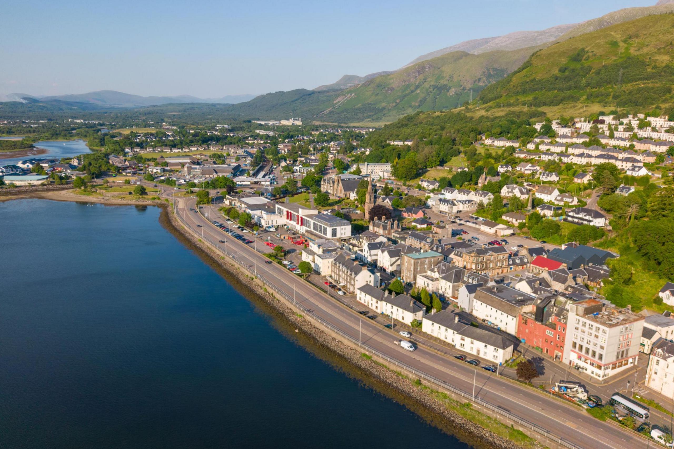 An aerial view of houses and other buildings of Fort William on the shores of Loch Linnhe on a sunny day.