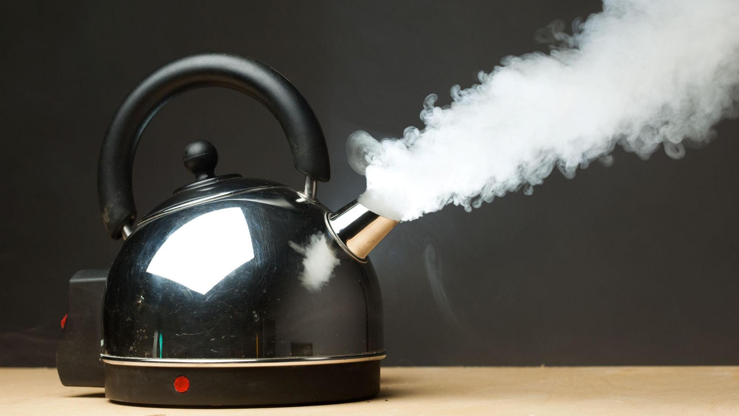 A silver and black electric kettle boiling