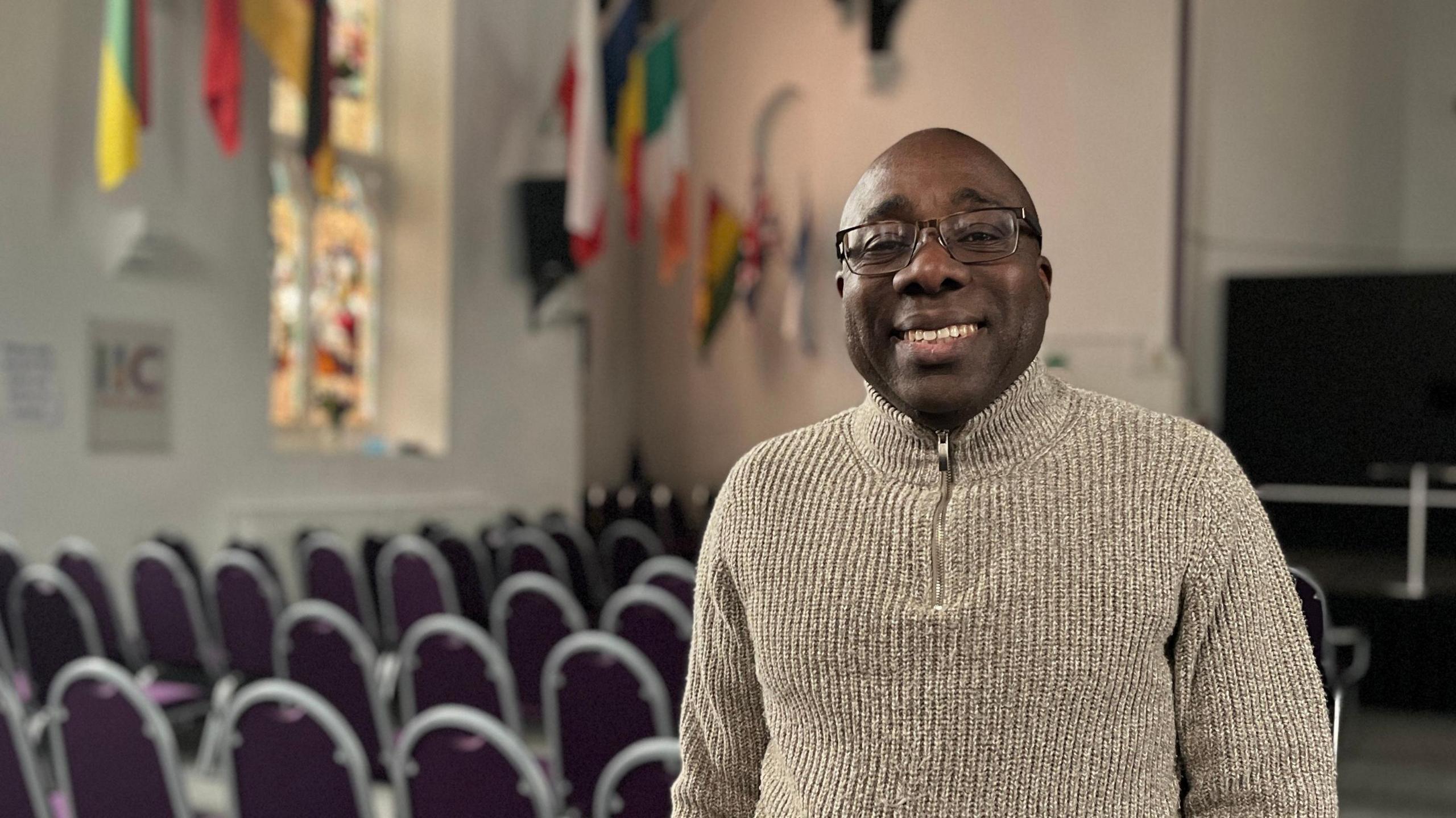 Reverend Harold Afflu stands inside an empty church, with flags on the wall