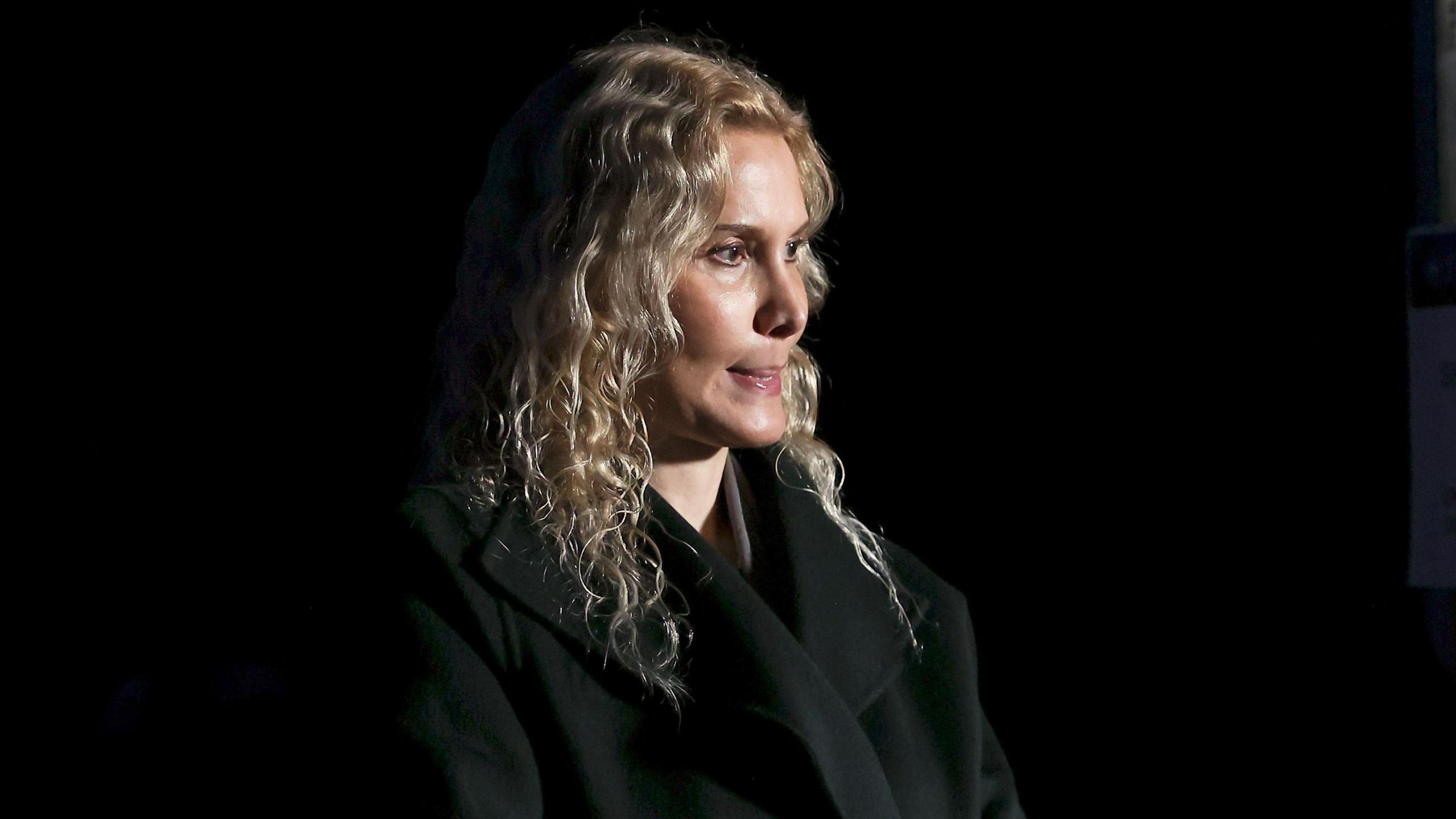 Blonde-haired coach Eteri Tutberidze in a black outfit against a black background