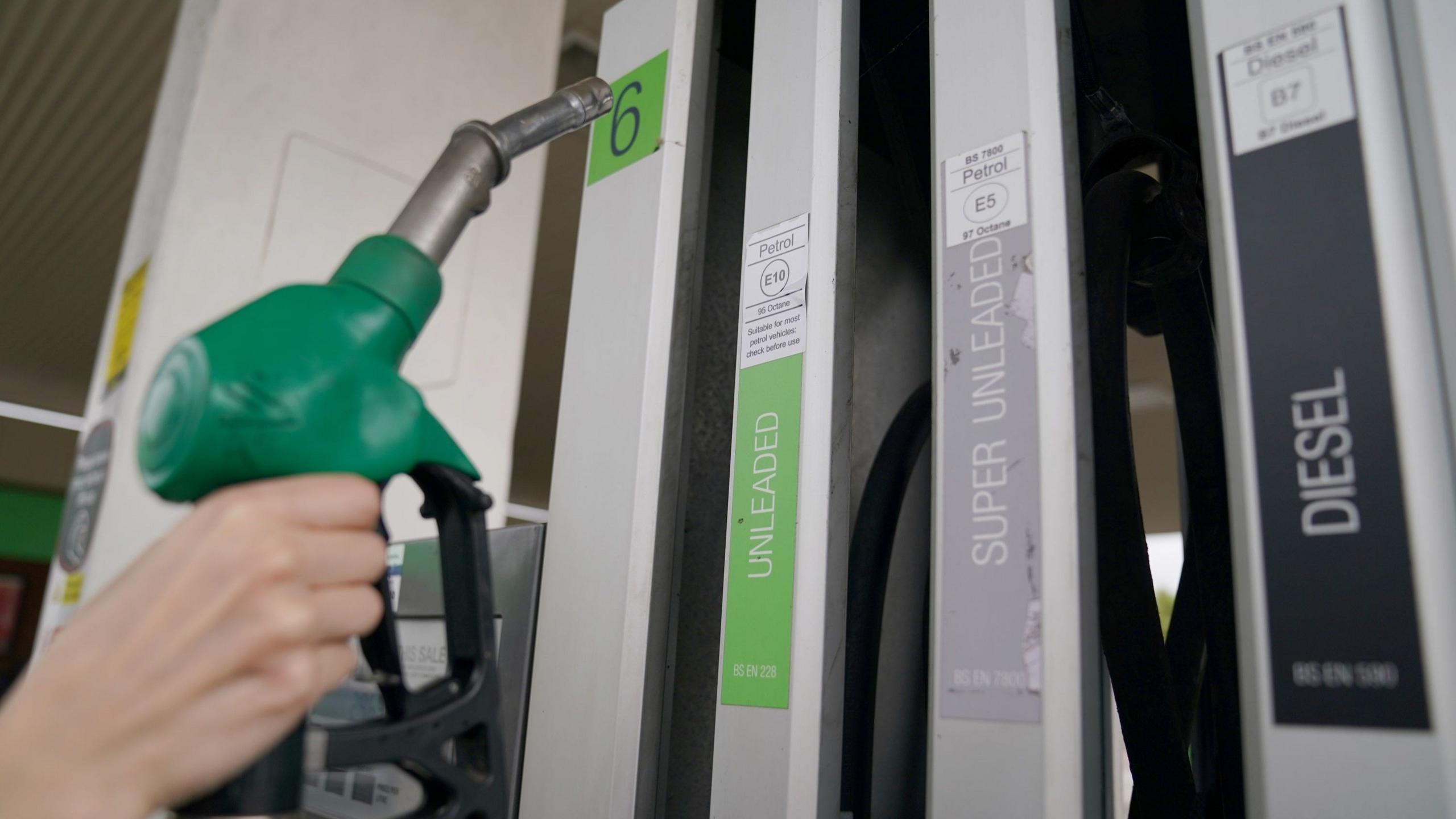 hand reaches for a green unleaded petrol pump on a forecourt
