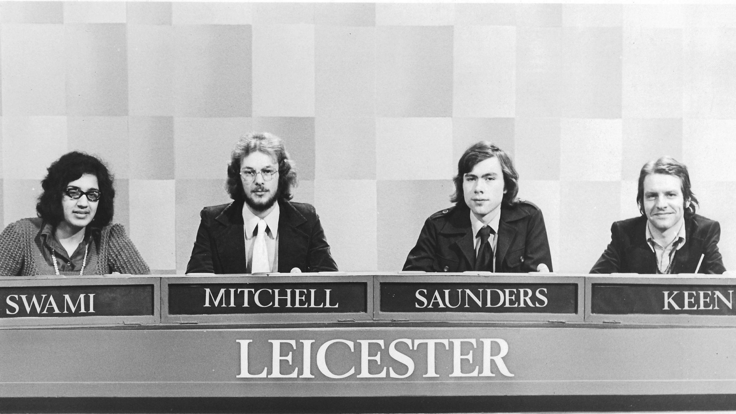 A black and white picture of a team from the 1970s, in formation with their names underneath, with three white men joined by one South Asian woman