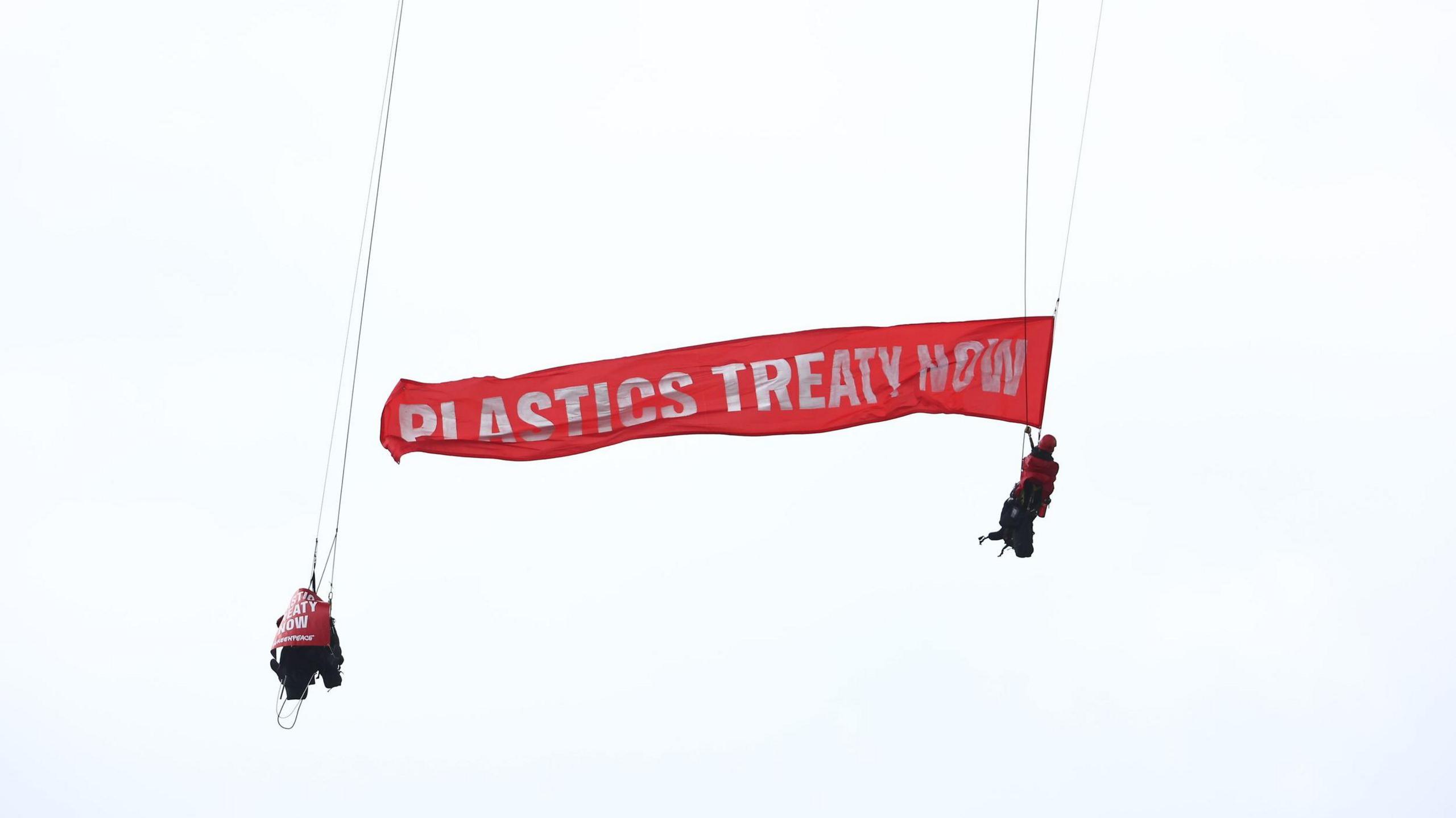 Two Greenpeace protesters displaying a banner reading 'Plastics Treaty Now' during the protest at the Forth Road Bridge.