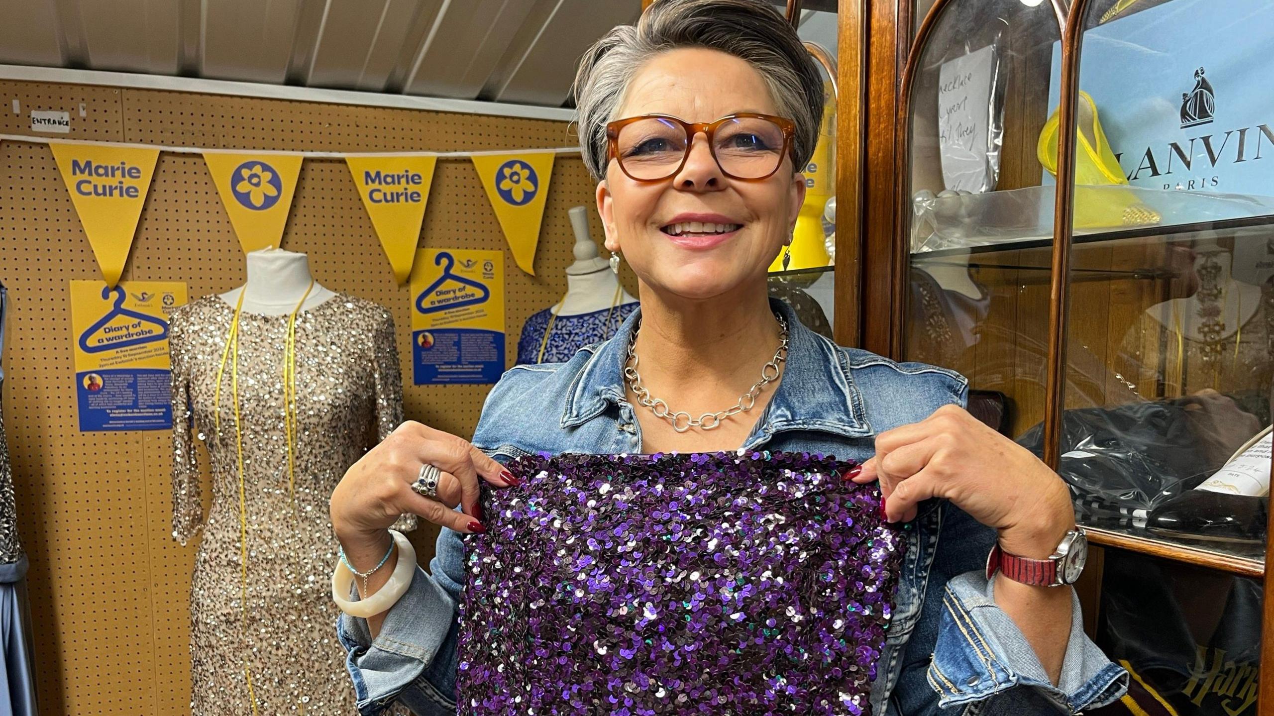 An auctioneer holds up a purple sequinned dress owned by actress Jane Horrocks