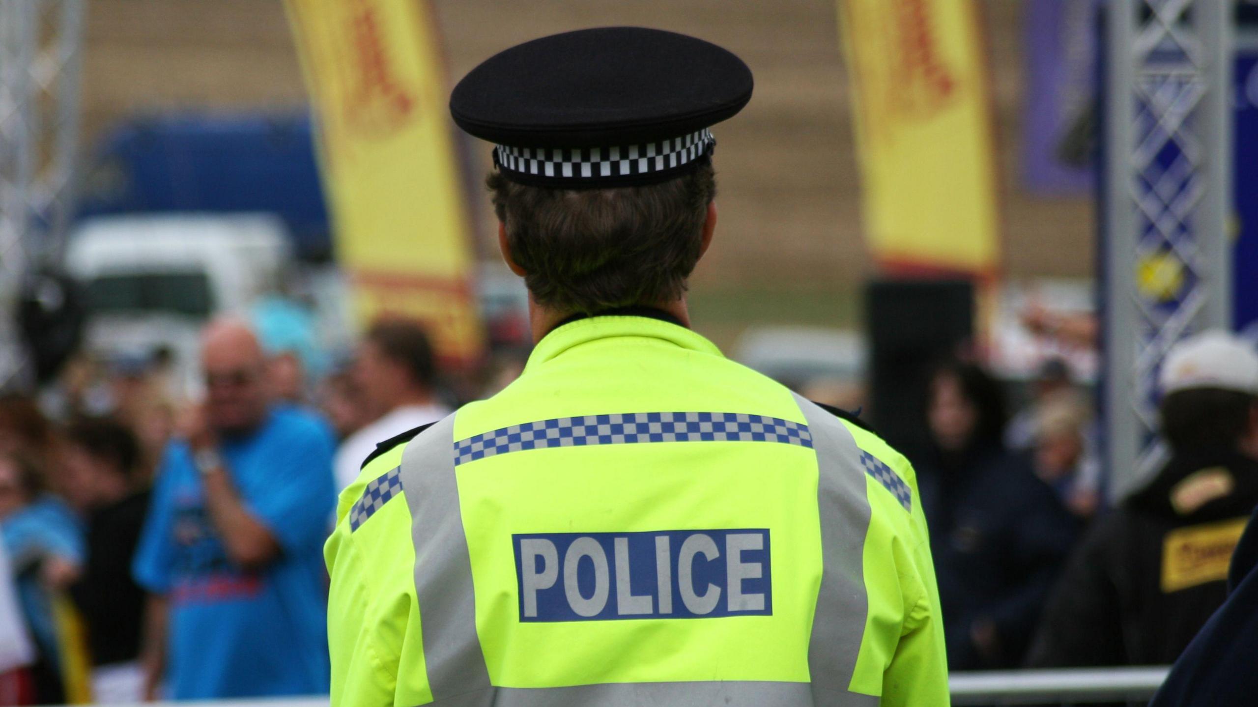 The back of a police officer in a high-vis jacket, looking out over a blurred crowd.