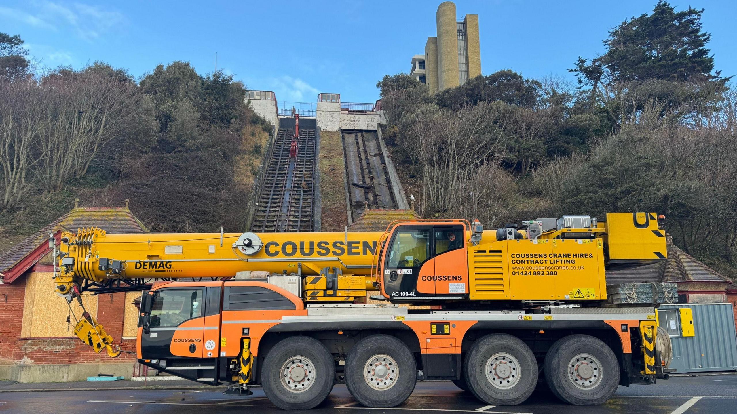 A large yellow and orange crane parked in front of the funicular. 