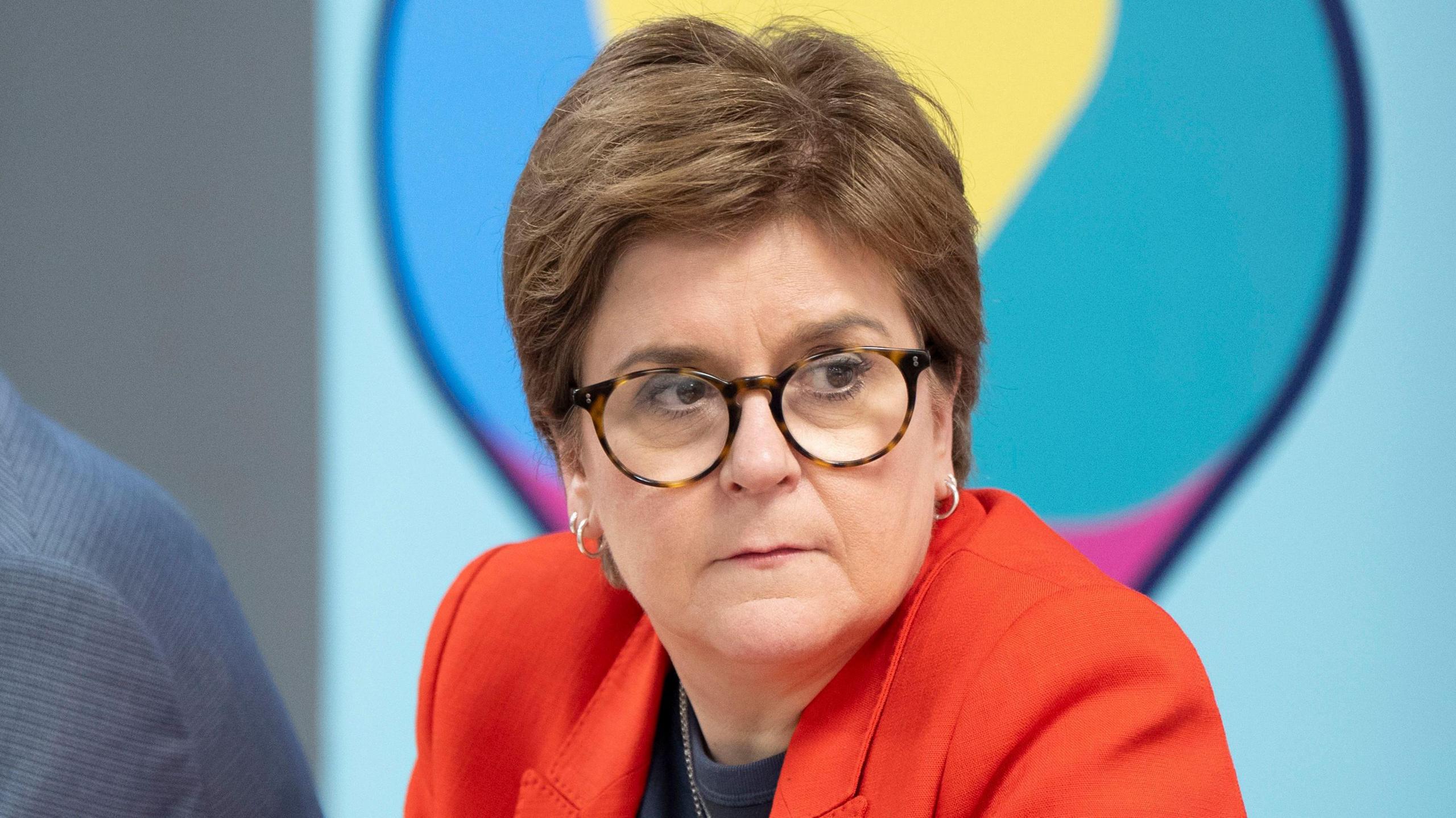 A woman with short brown hair and glasses looks off into the distance with a serious expression on her face. 