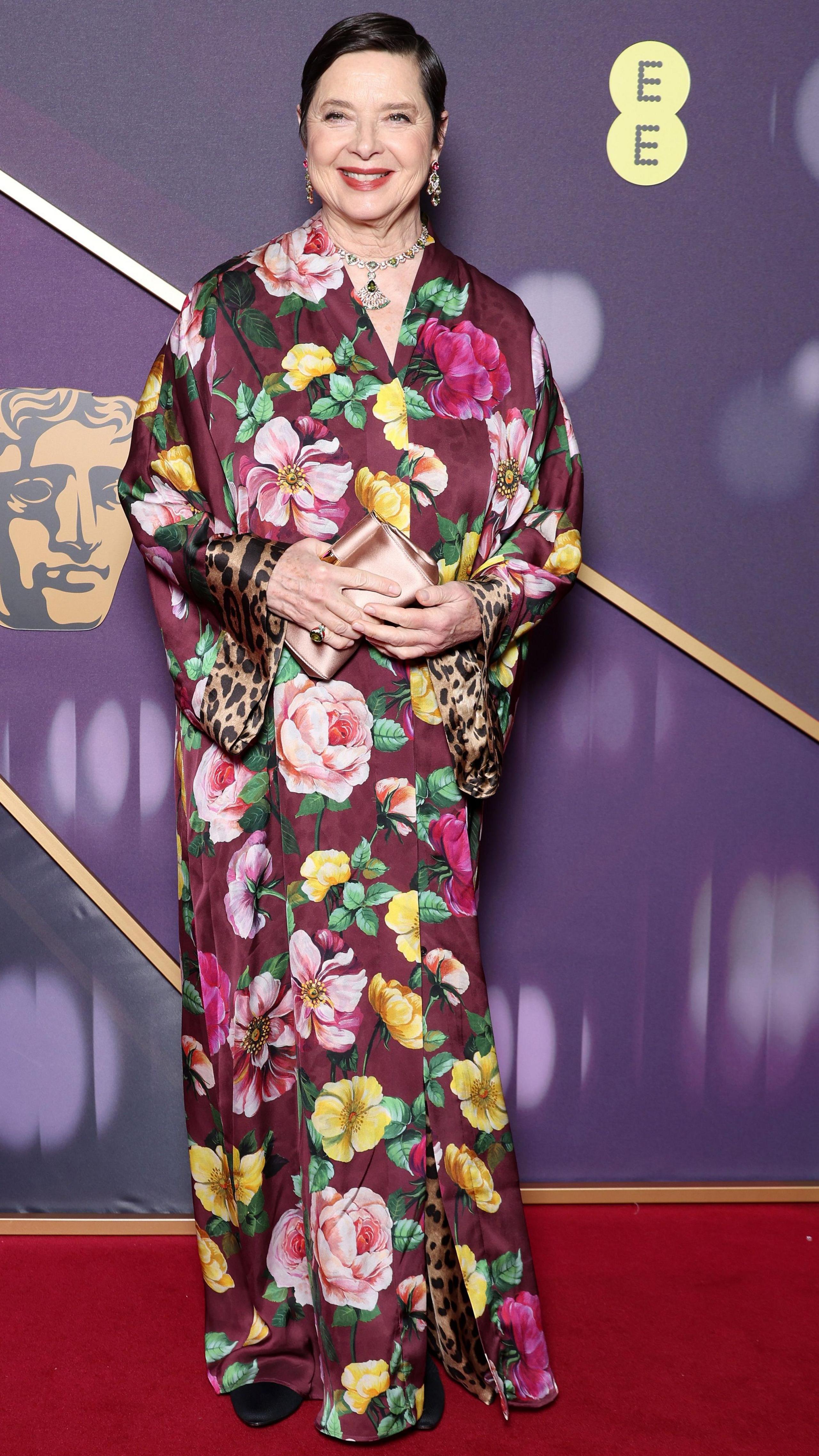 Isabella Rossellini in a purple, pink and yellow floral long, floaty dress with flashes of leopardskin