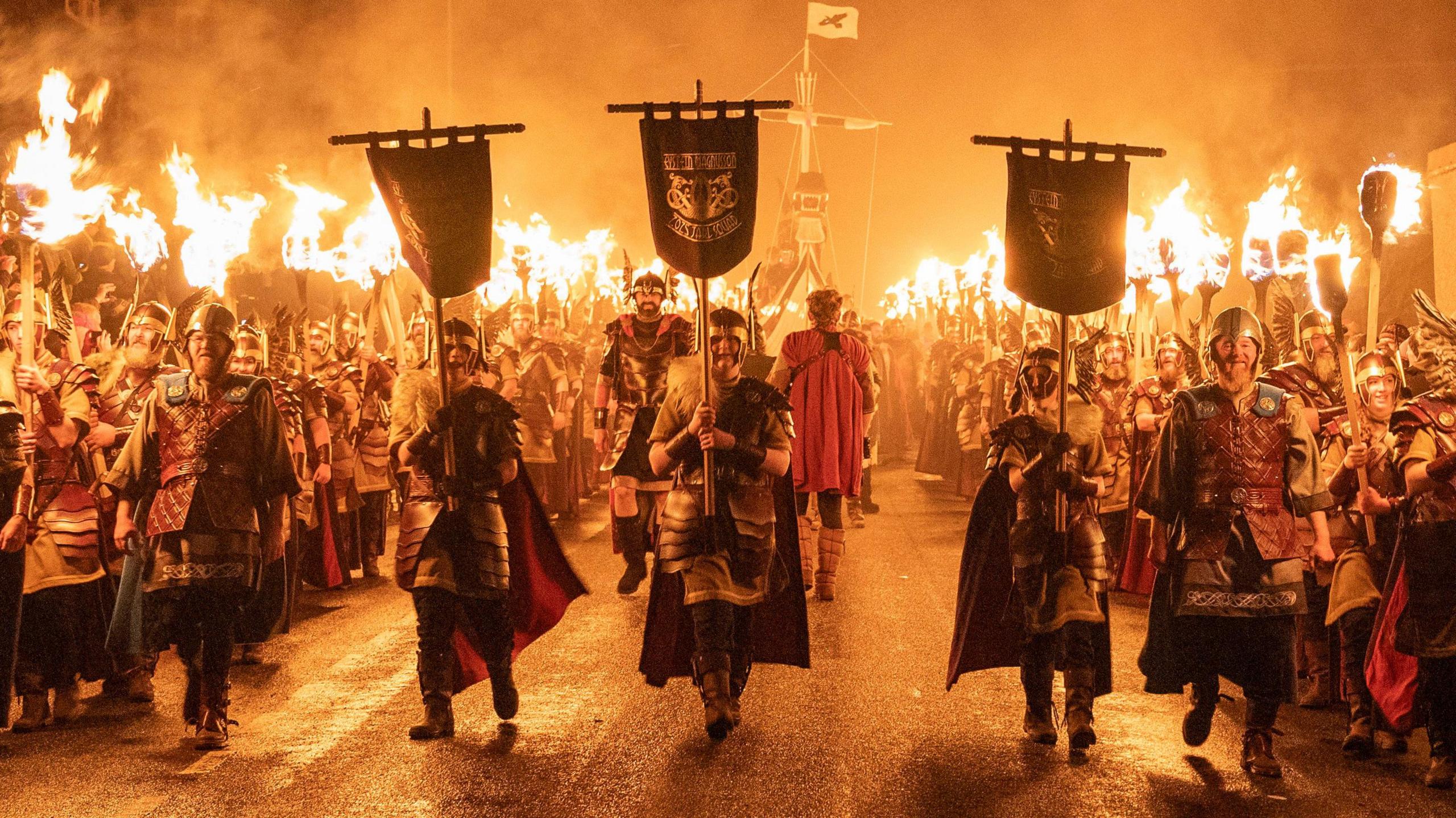 people parading down street in shetland with flags and burning torches