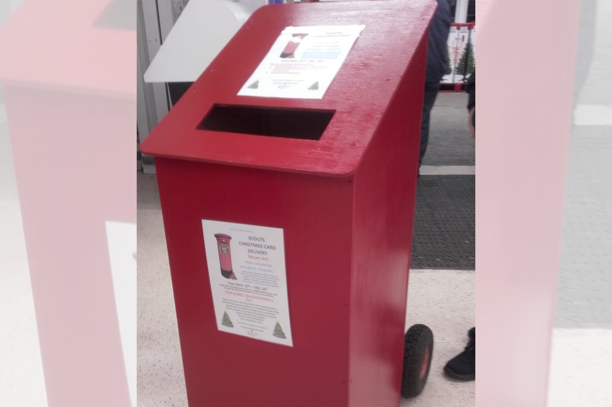 A red wooden post box placed inside somewhere. It has a couple of posters printed on it.