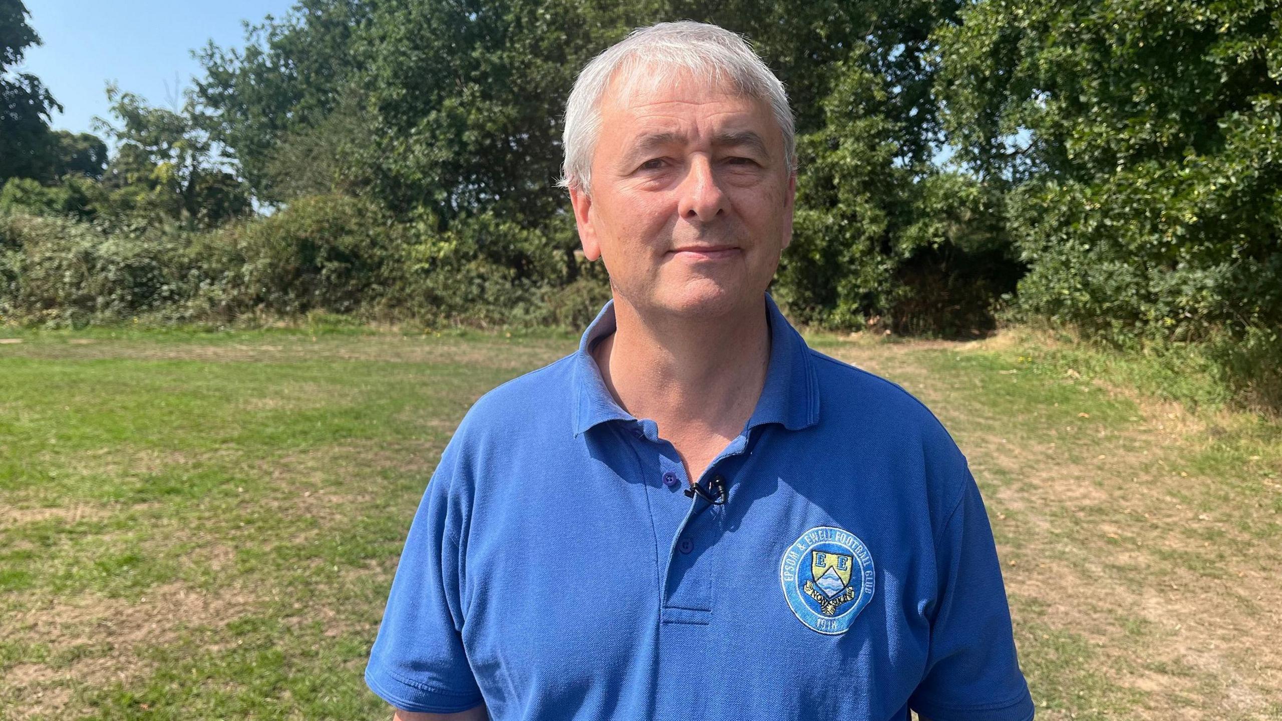 Richard Lambert standing in a field in front of trees in the background and clear blue sky