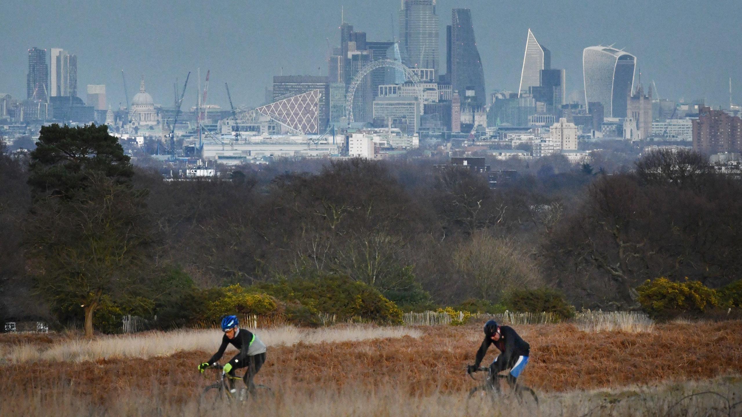 Two men cycling on road bikes in Richmond Park, with the skyline of London miles away in the distance.