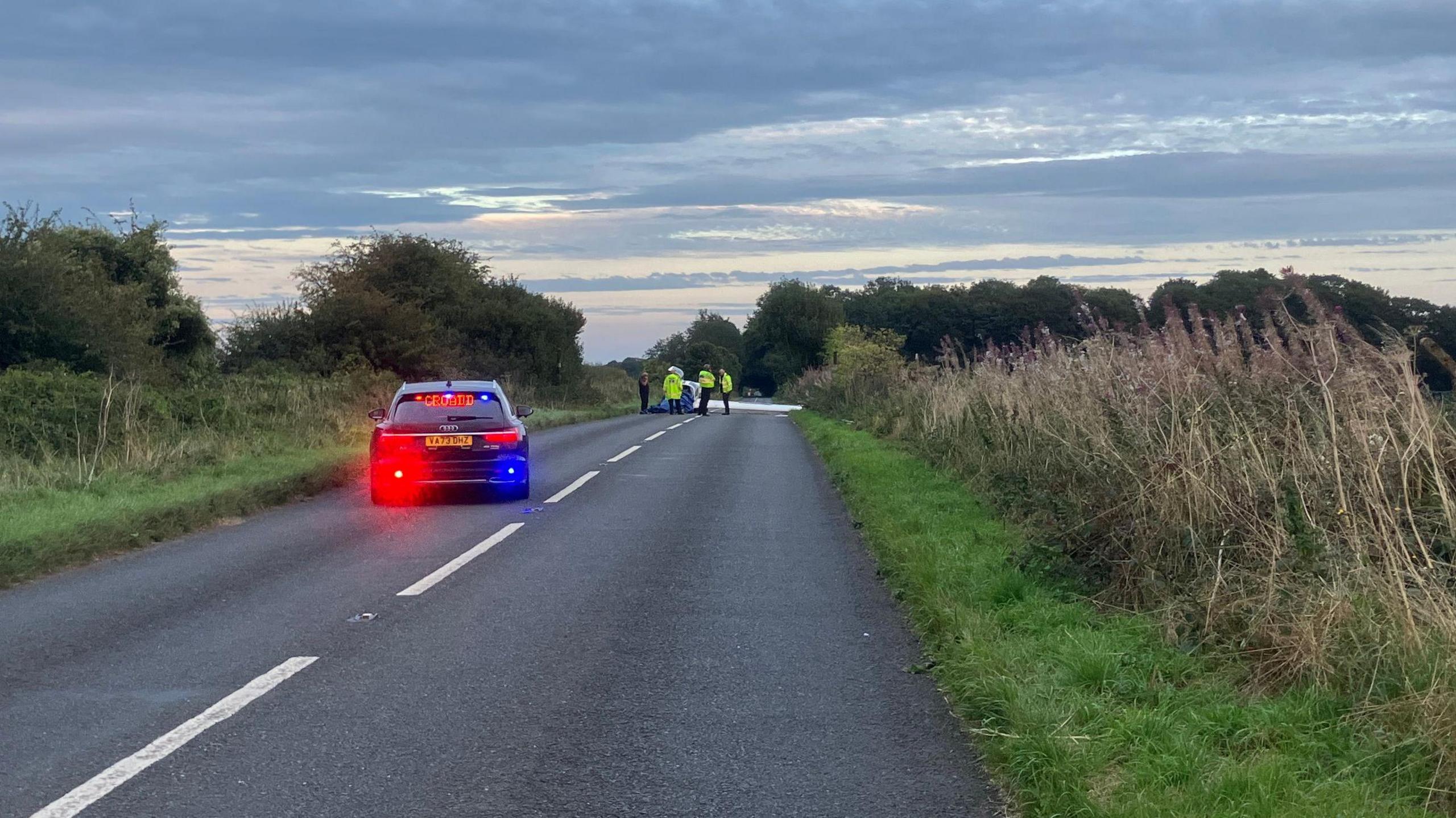 A police car parked behind some traffic cones on a country road