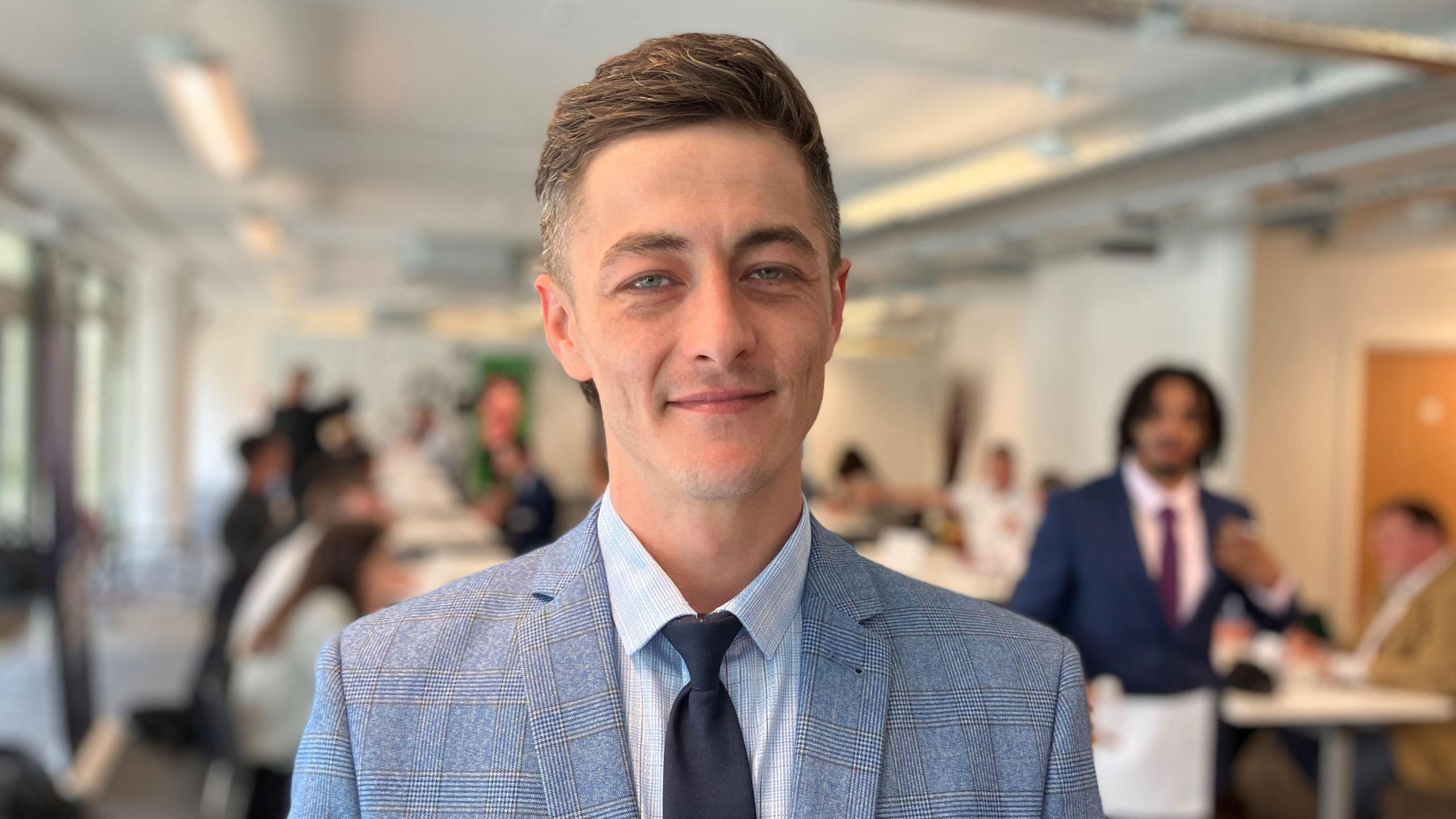 Head and shoulders shot of Liam Meredith who is wearing a blue checked suit and dark tie