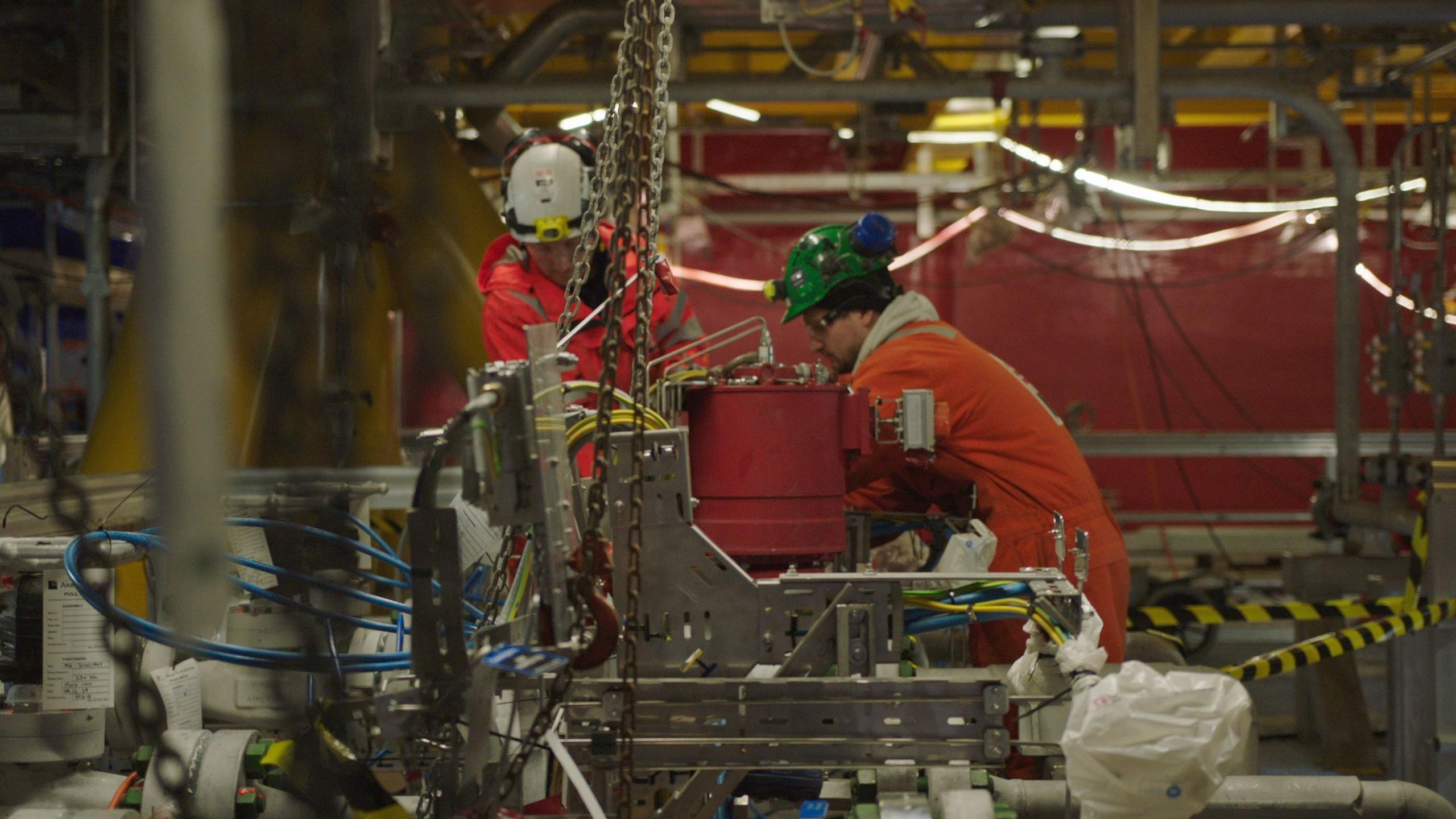 workers in orange overalls operate heavy machinery