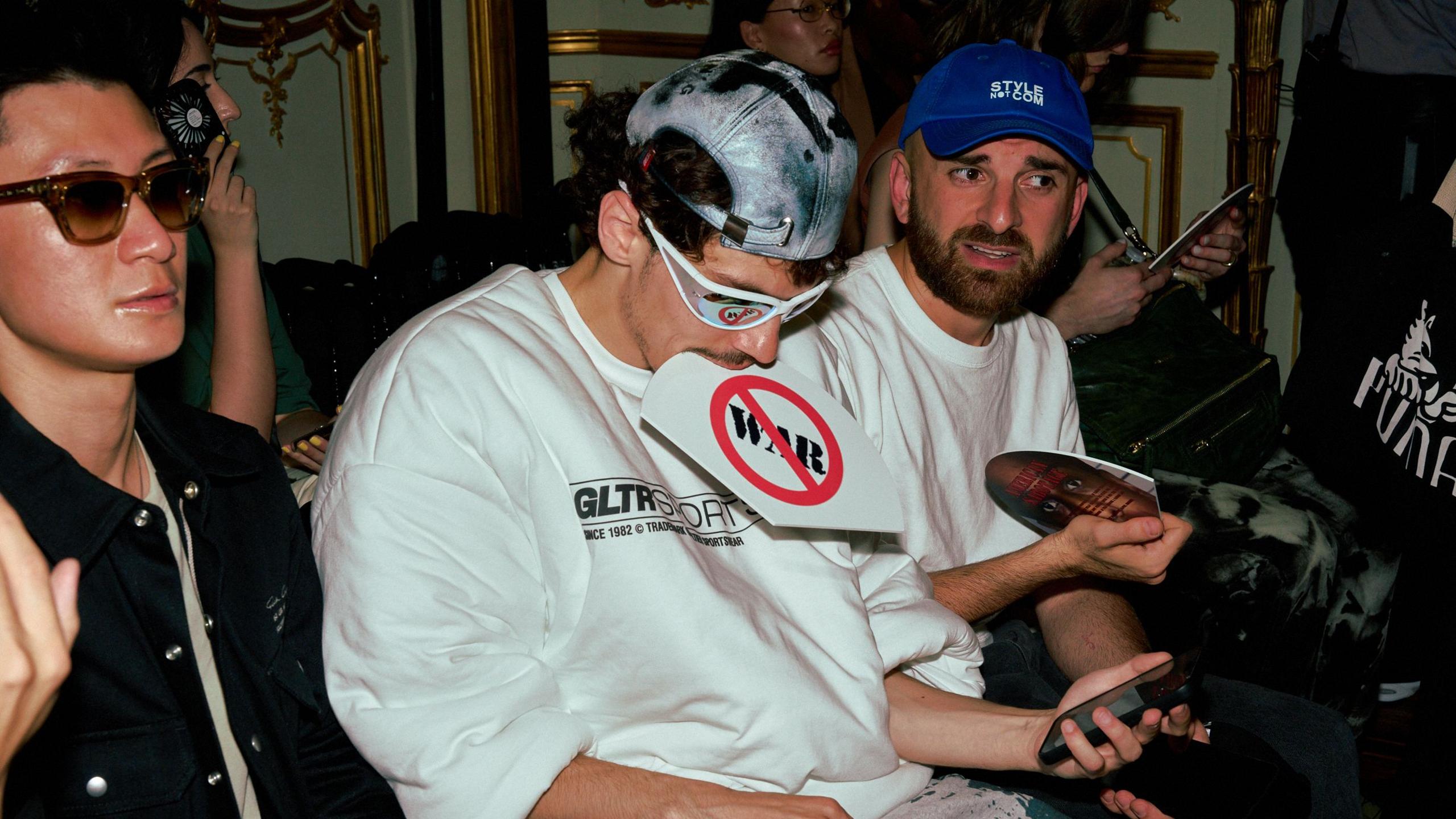 Man wearing sunglasses sits with fan between his teeth