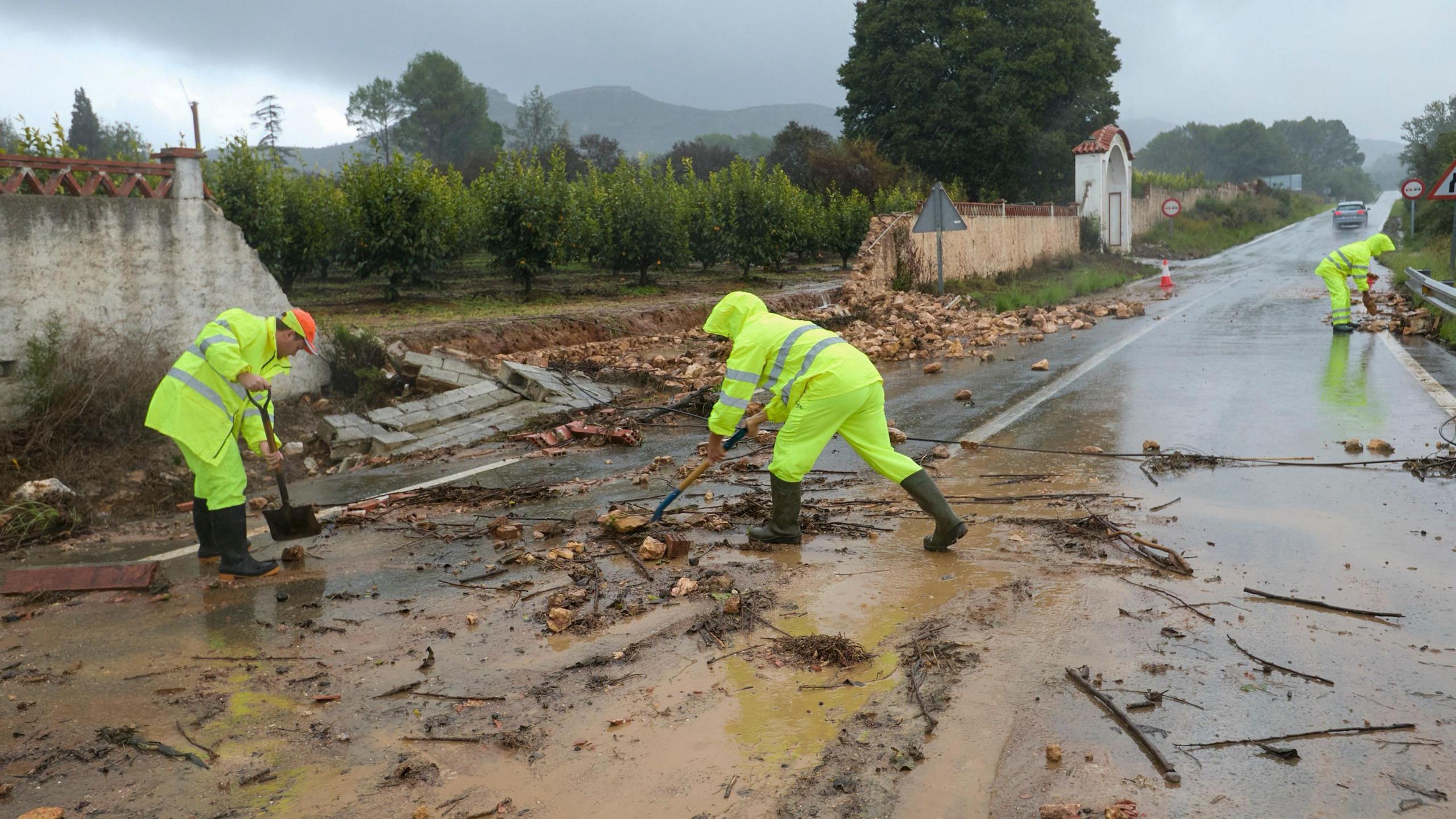 People in high-vis clothing try to clear roads of debris after flash flooding.