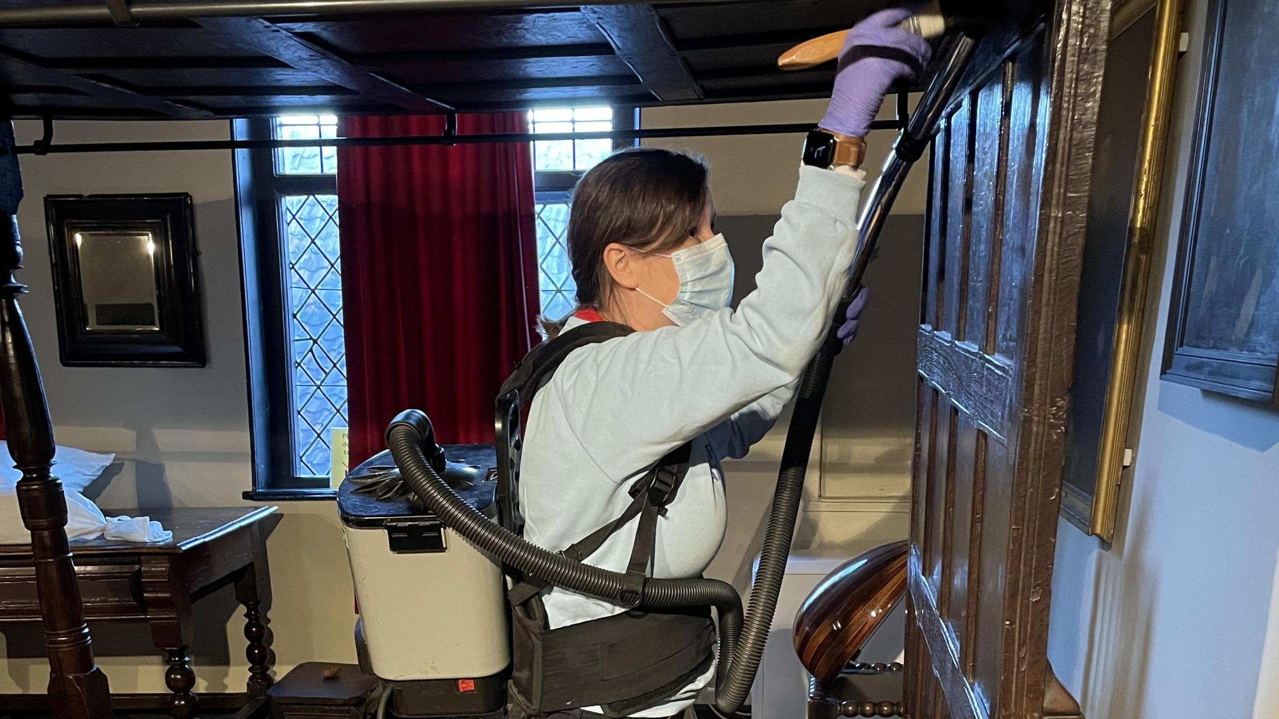 A person cleaning a bed at Strangers’ Hall Museum