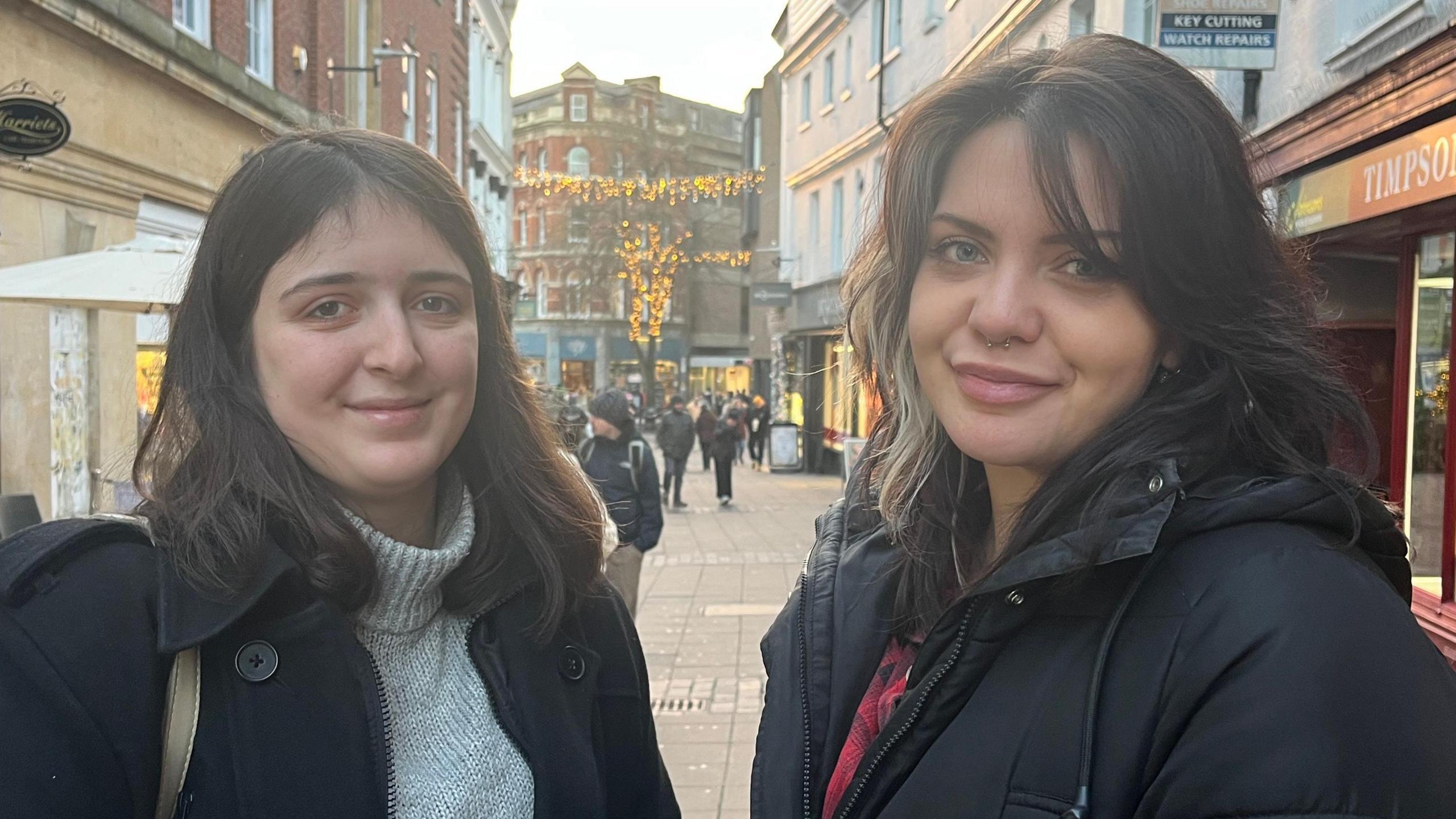 Bethany Patterson is 21 and pictured on the left, with a grey jumper holding a coffee. Lauren Herring, who is 29, is on the right with a black coat, dark hair, smiling at the camera