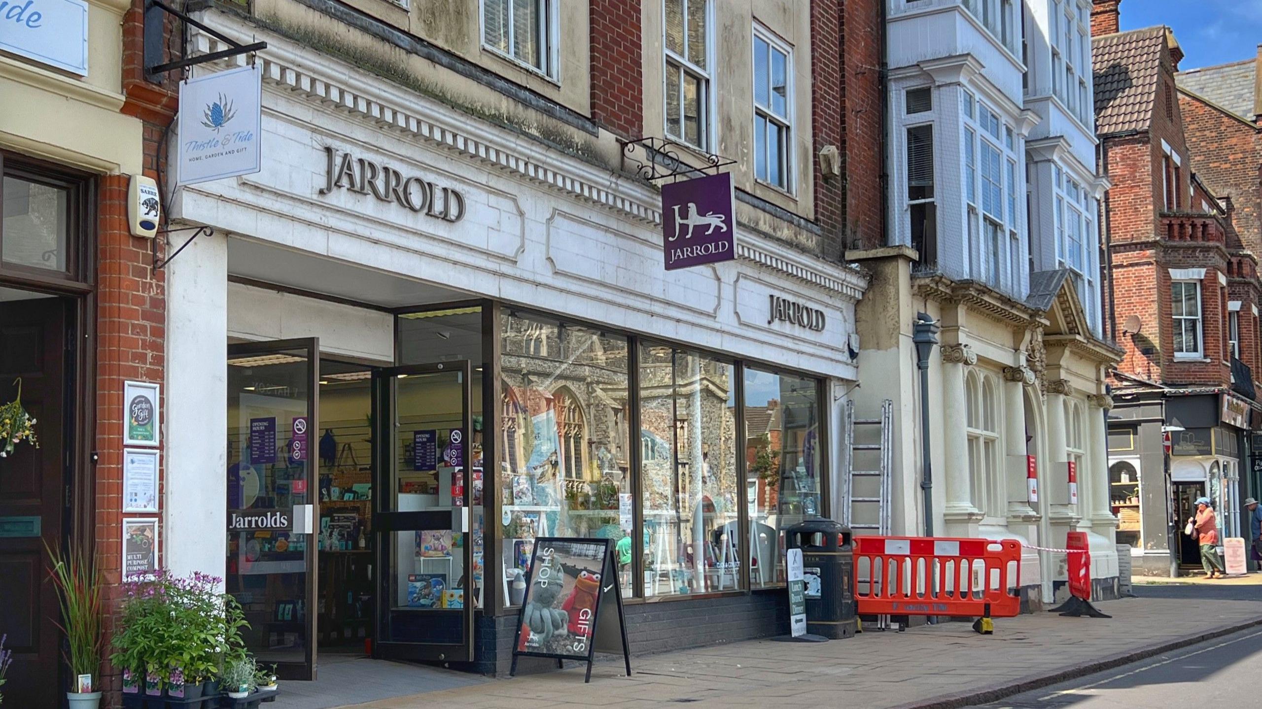Line of shops showing the facade of the Jarrolds book store in Cromer, with an A board outside and some road work barriers further along
