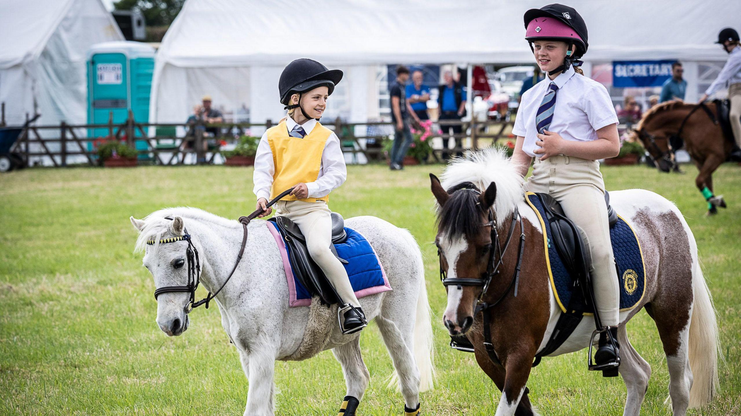 Two young girls on ponies at an agricultural show