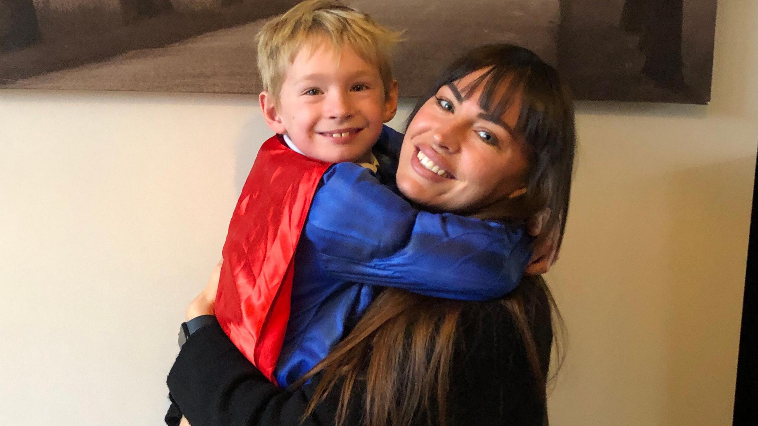 Fletcher is hugging his mum, Lori. He's wearing a Superman costume.