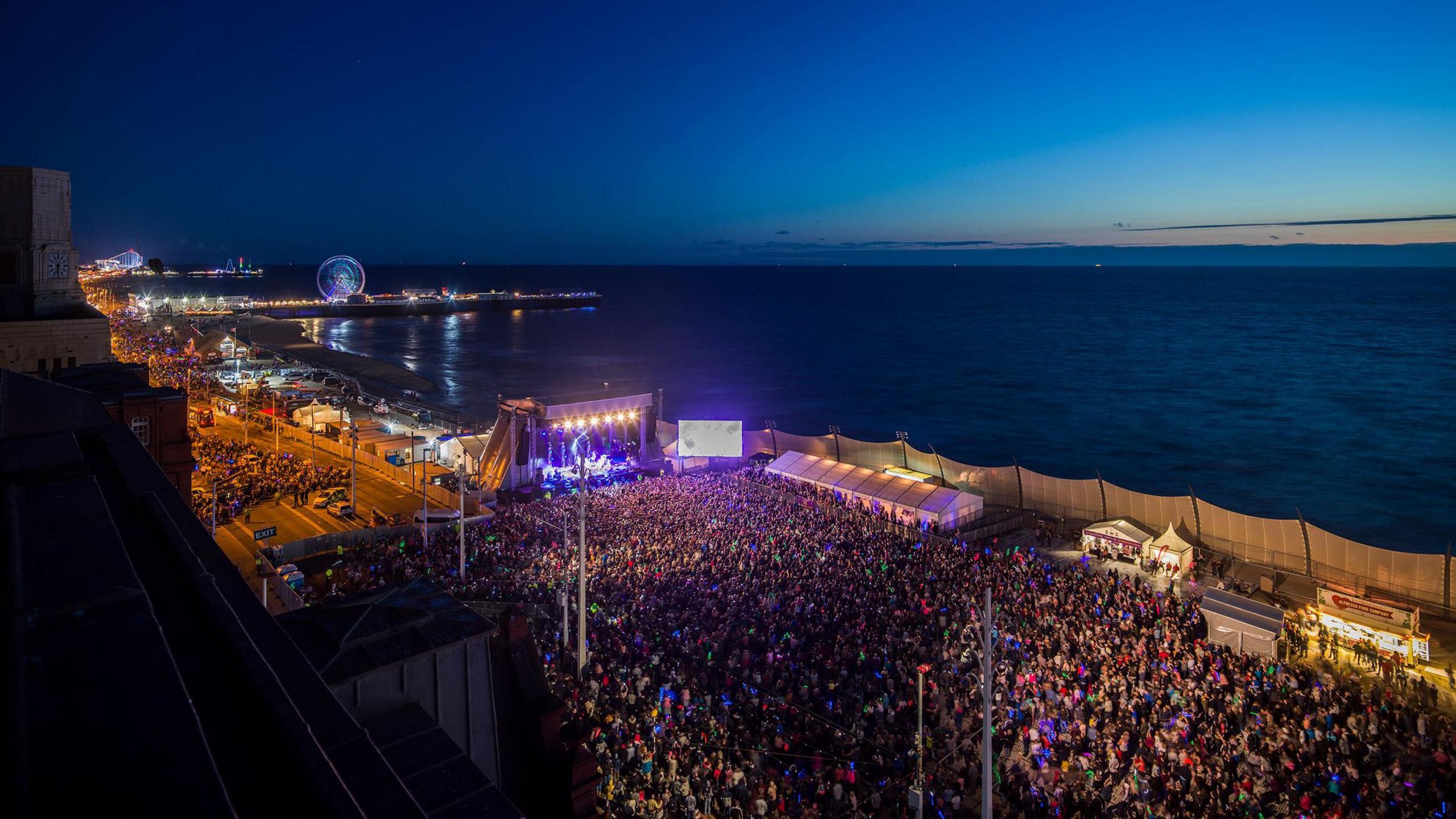 Thousands of people pack Blackpool Promenade as the sun sets over the sea.