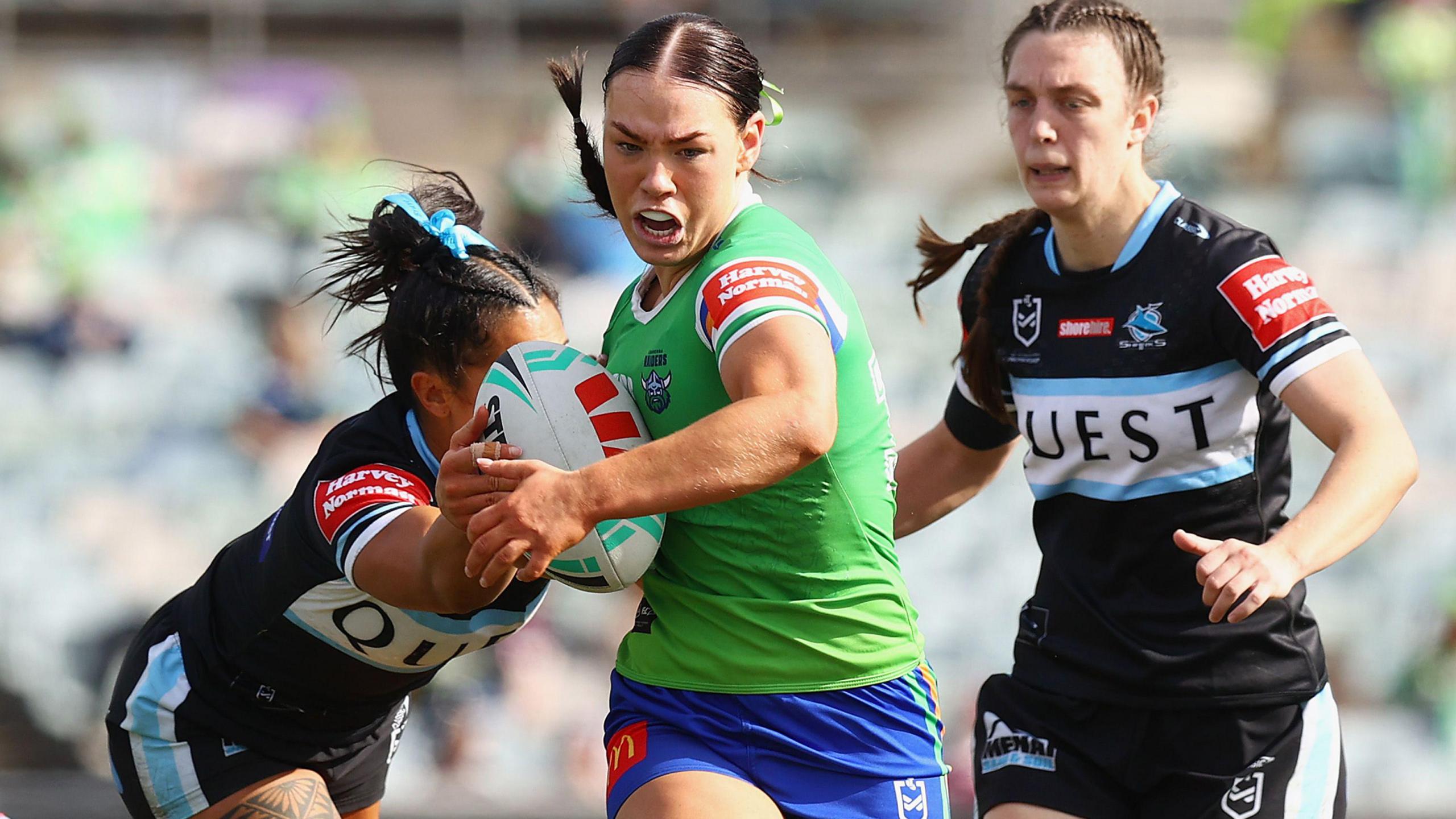 Hollie-Mae Dodd runs at a gap between two Cronulla players as one reaches out in attempt to tackle her, swivelling her upper torso to evade being caught