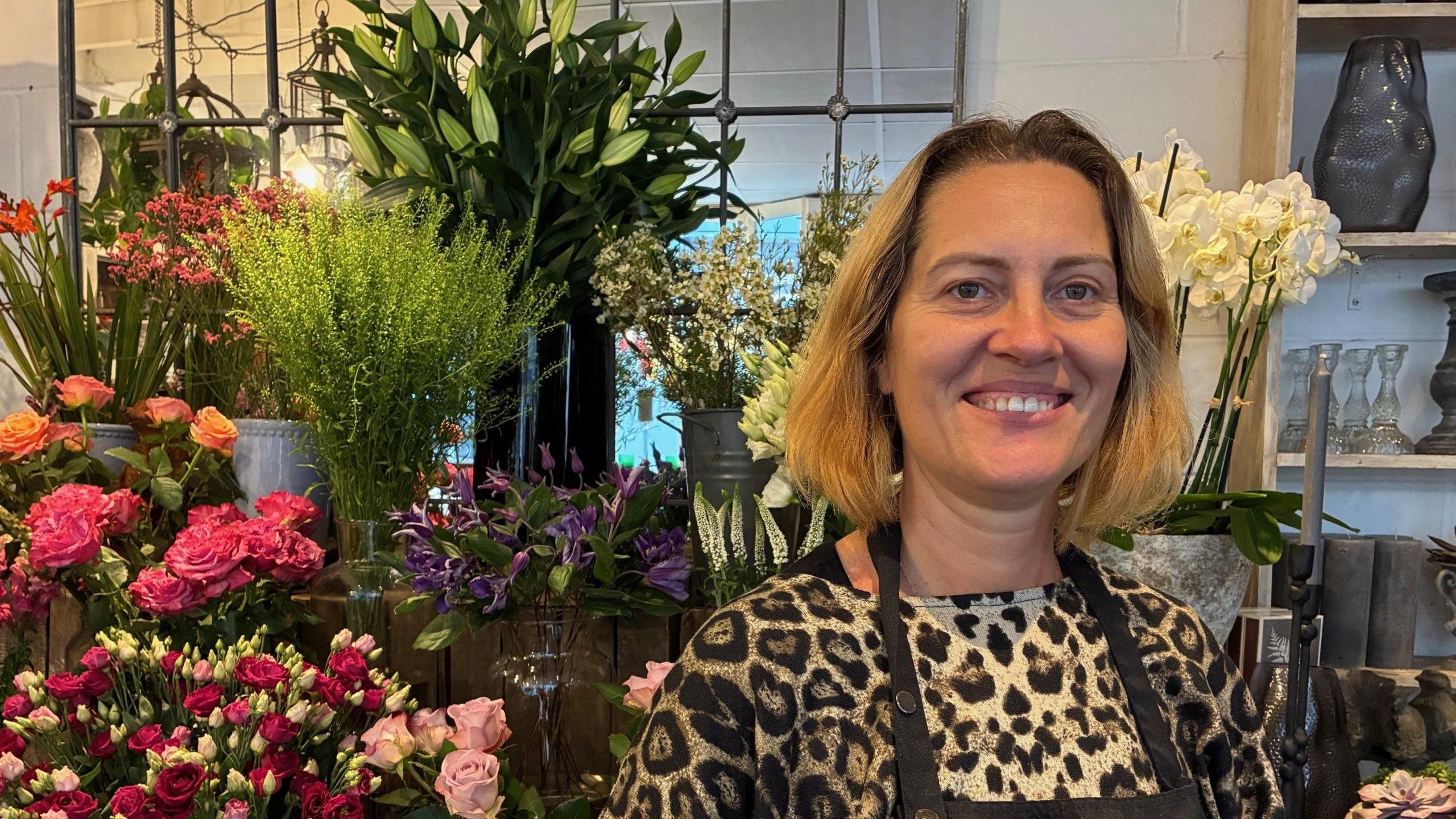 Terezai Takacs stands in front of a display of a range of flowers, mostly roses.