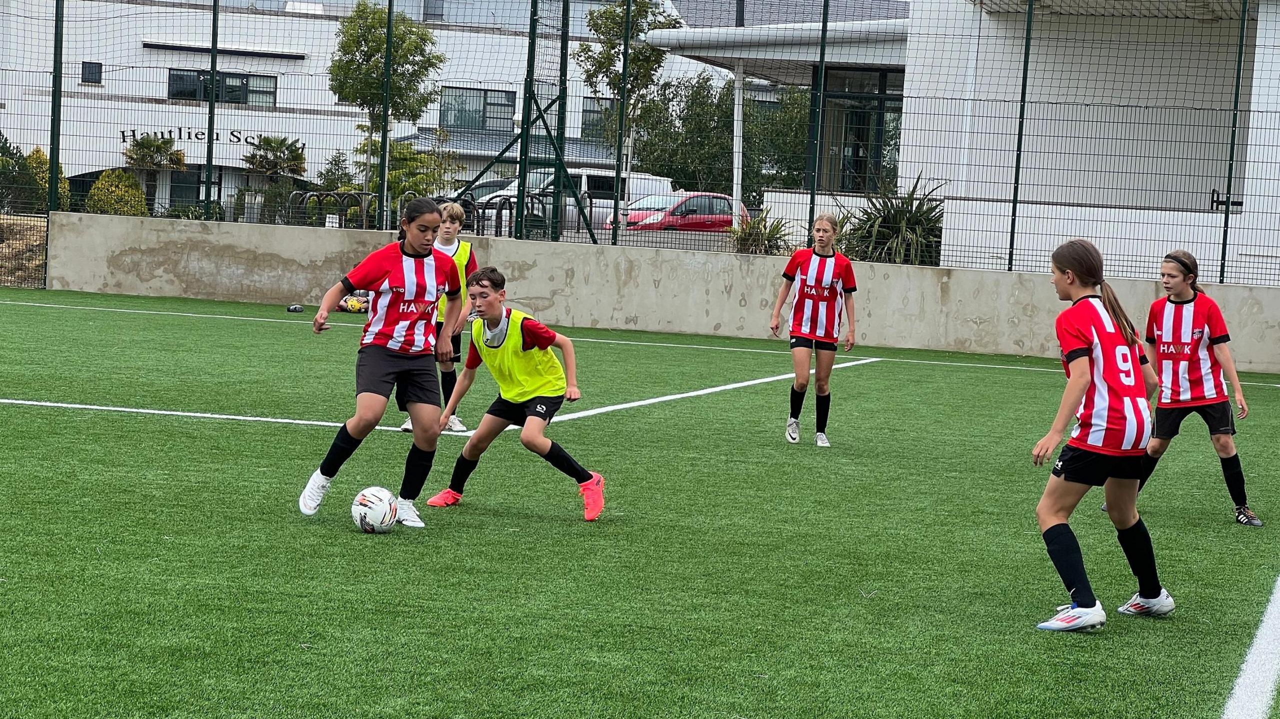 A girl is about to pass the ball to a team mate as a boy tries to close her down