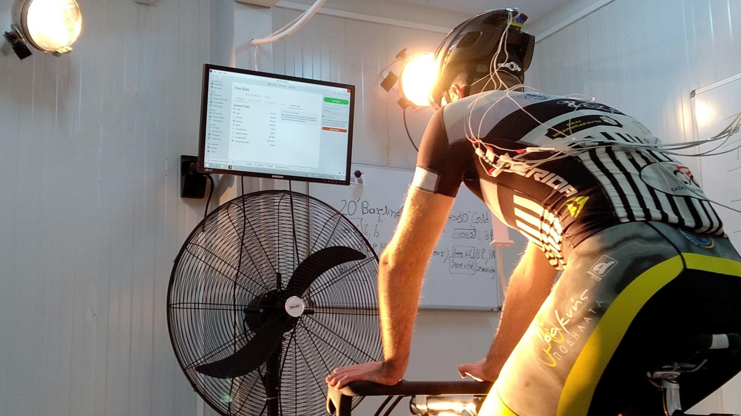 A cyclist on a static bike undergoes a test, with cables running from his helmet and shirt.