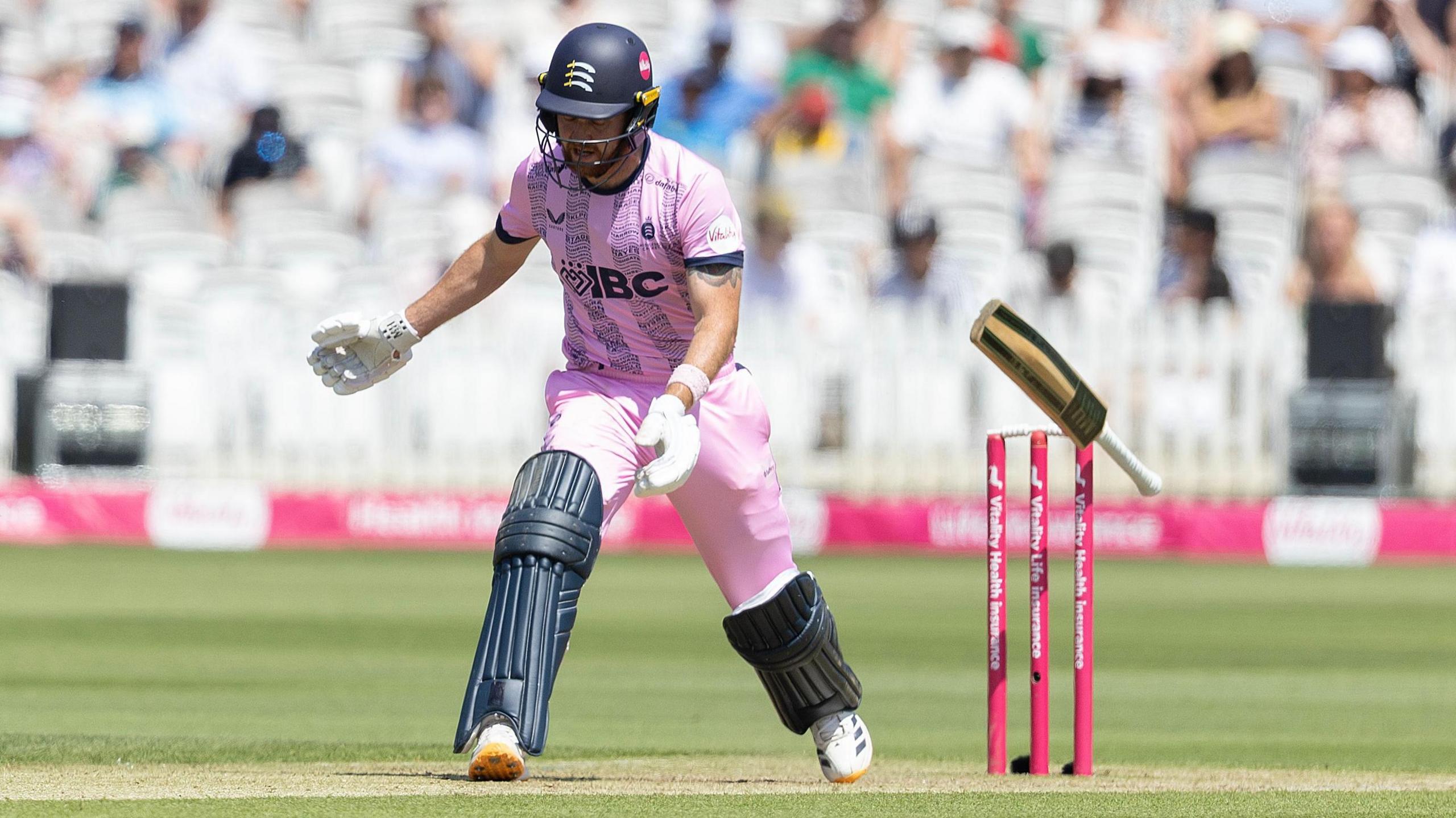 Ryan Higgins, in the pink strip of Middlesex, loses grip of his bat which is about to hit the wicket