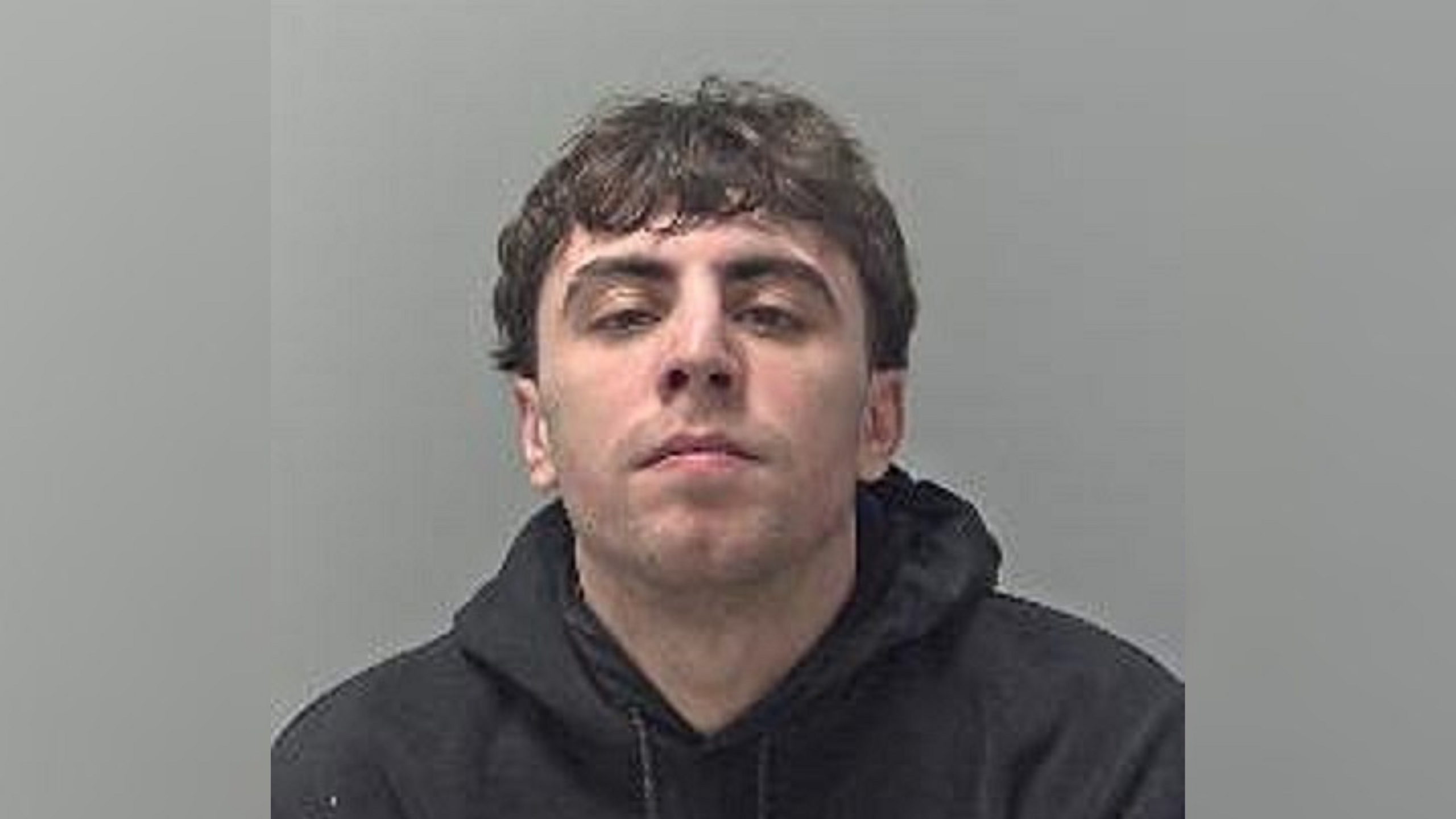 A mugshot of Simon Jones. He is wearing a black hooded top and looking directly into the camera.