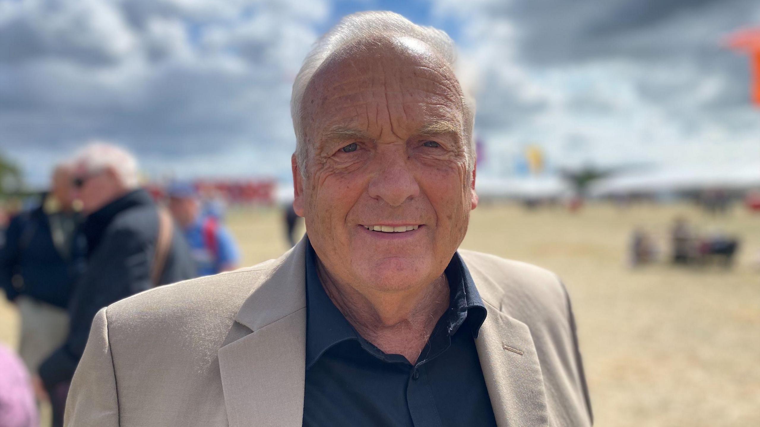 Victor Hughes yn gwisgo crys glas tywyll a siaced frown.